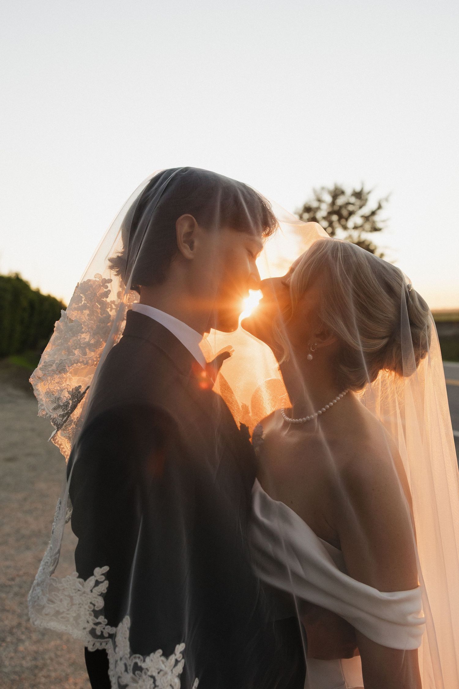 Silhouetted newlyweds share romantic kisses at sunset with bride's veil flowing in golden light.