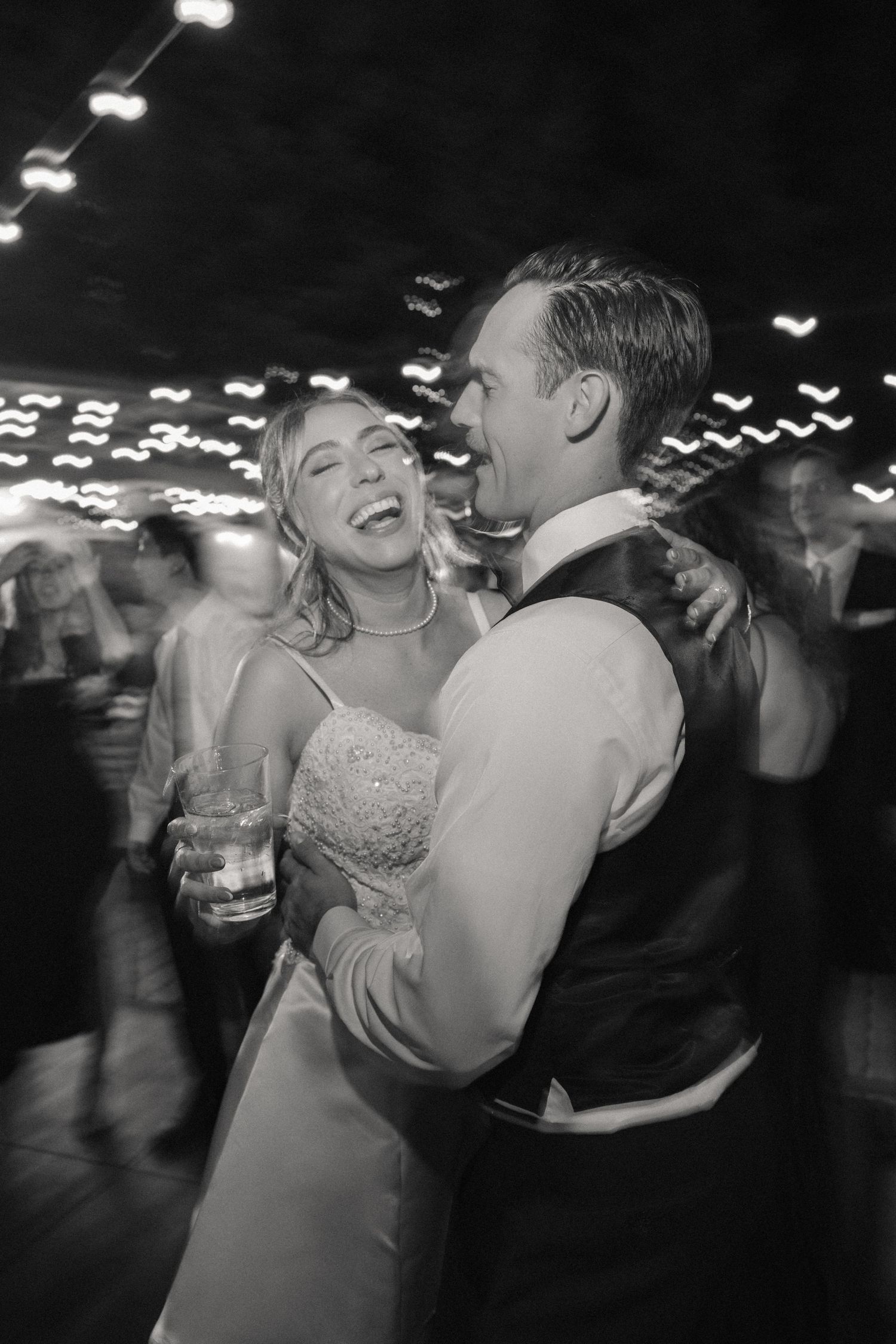 Black and white photo of a couple dancing and laughing together at their wedding reception.