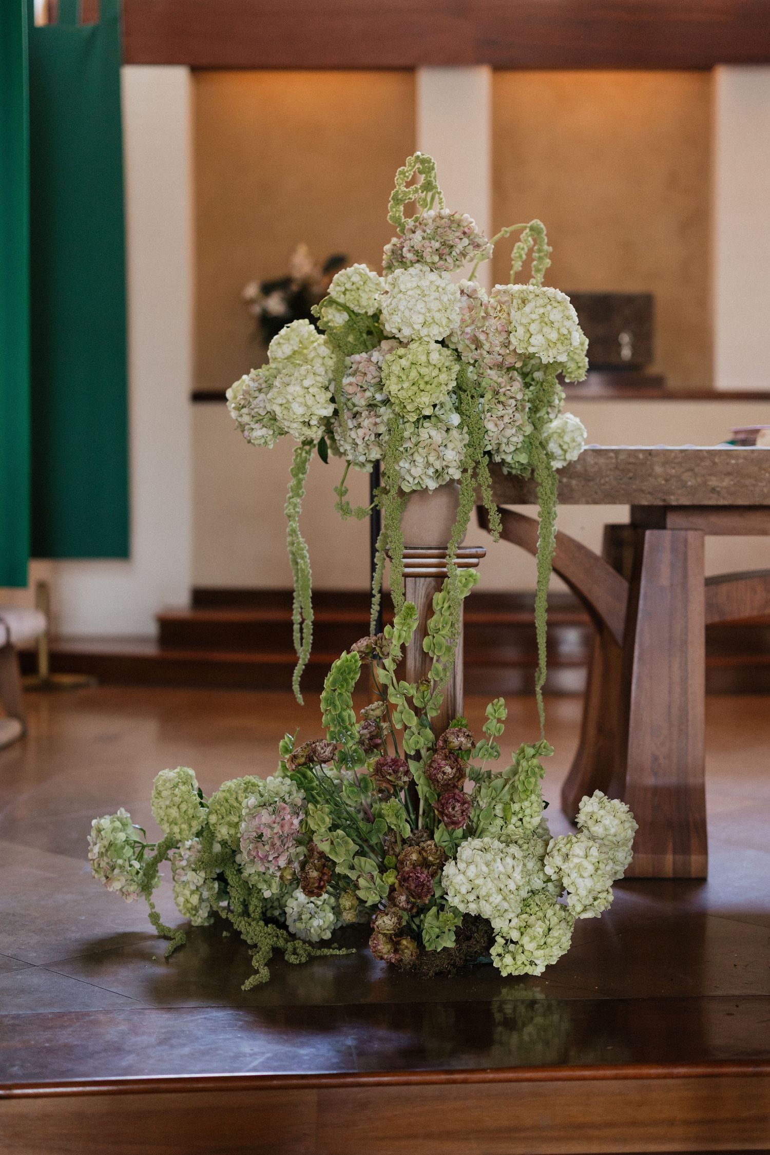 Elegant floral arrangement of green and white hydrangeas cascading down a wooden pedestal.
