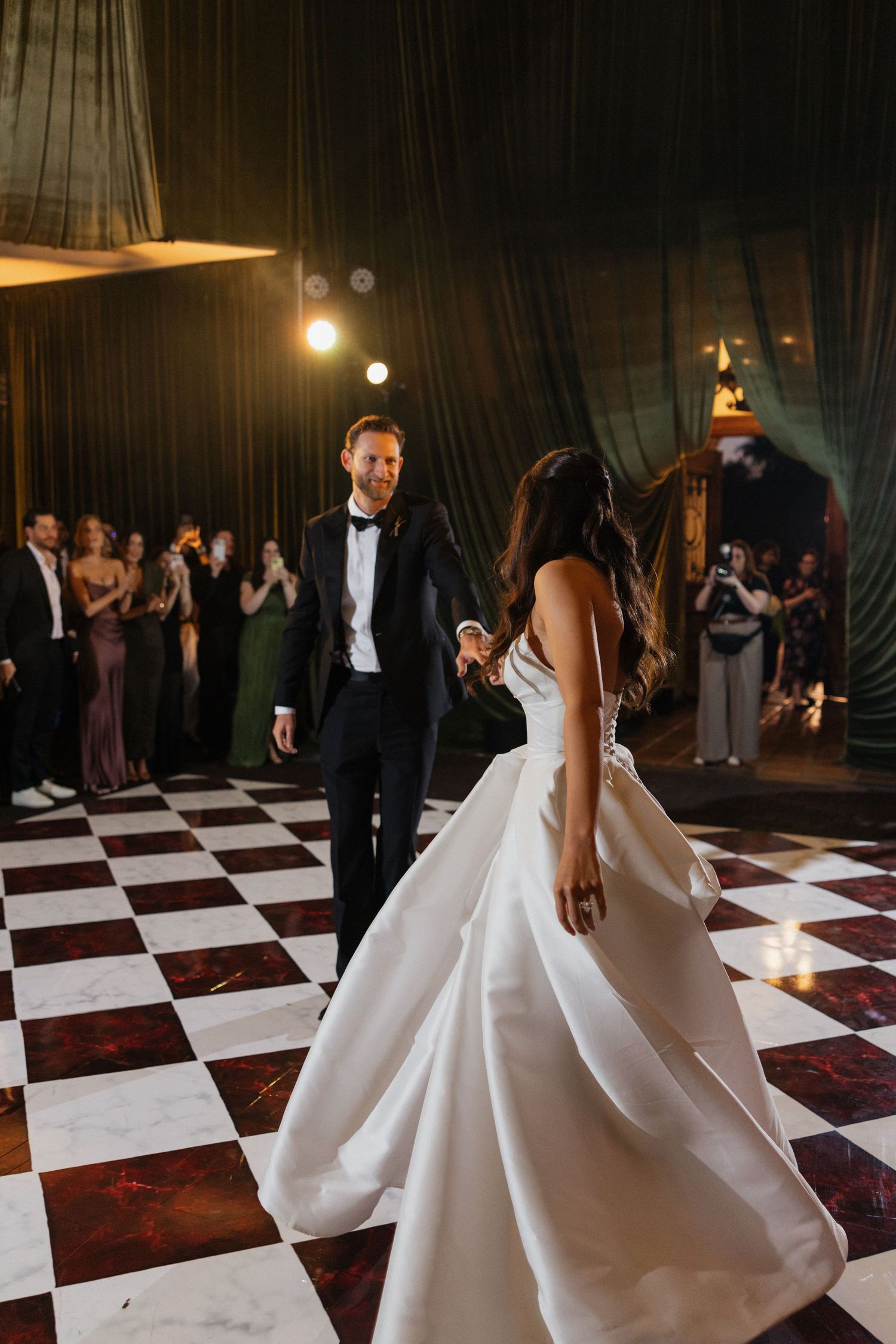 A couple dances elegantly on a black and white checkered dance floor at their wedding reception.