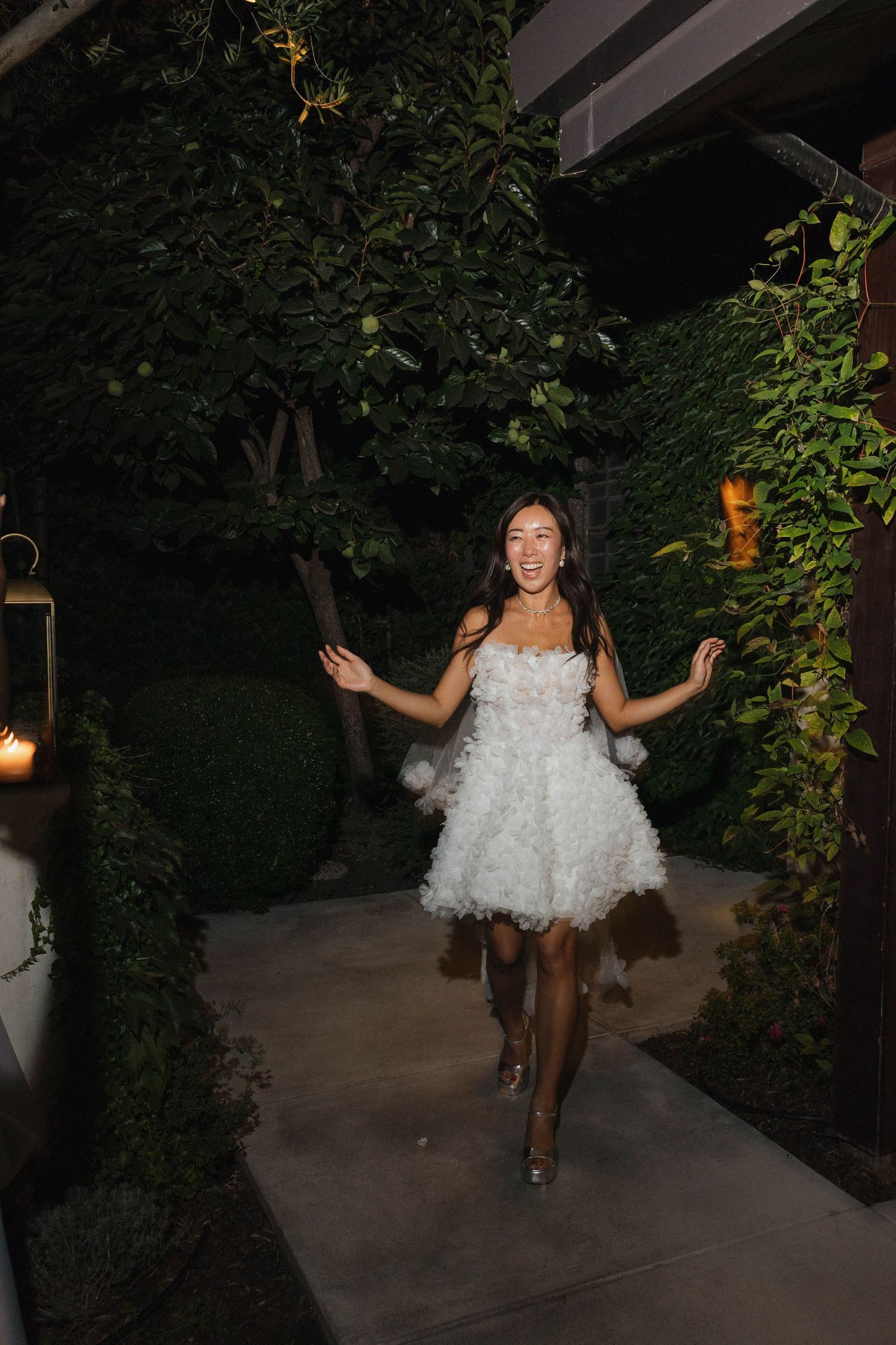 A person in a white ruffled dress dances joyfully on an outdoor patio at night.