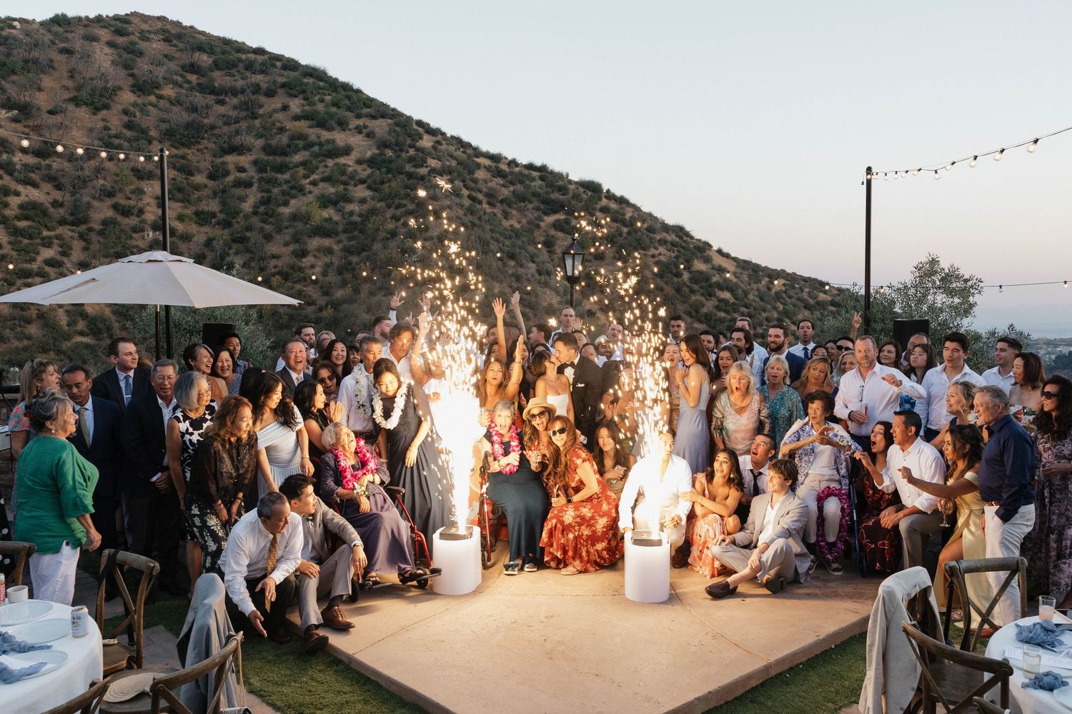 Panoramic view of an outdoor wedding reception with string lights and mountain backdrop at sunset.