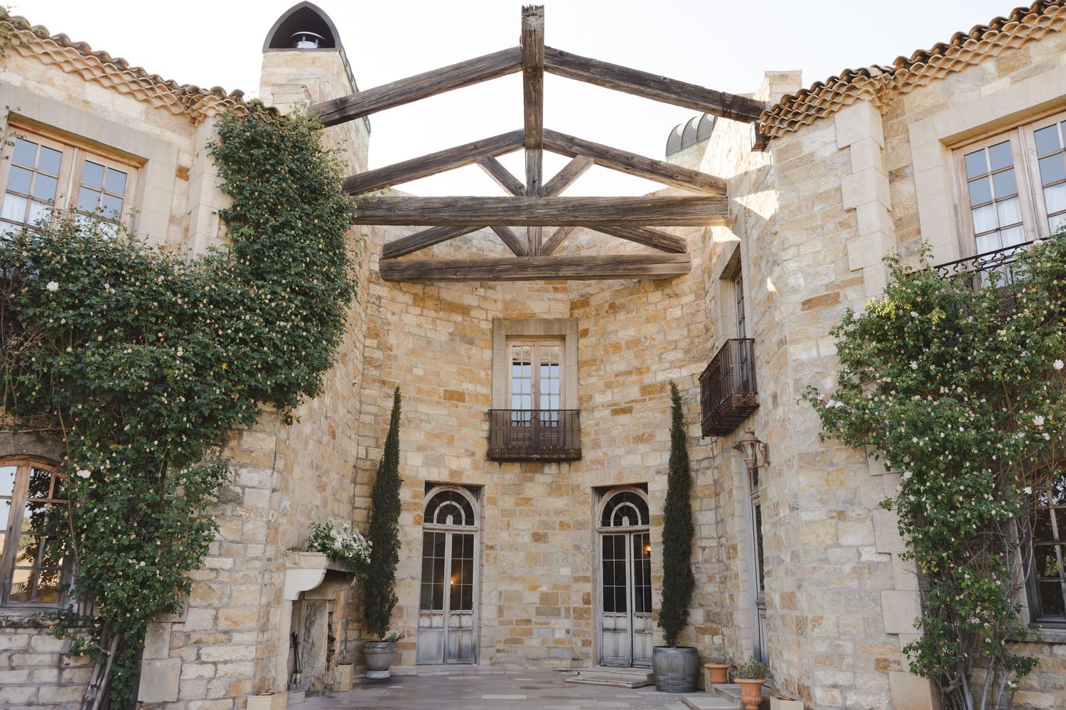 Rustic stone building entrance with wooden beams and climbing ivy on Mediterranean villa facade.