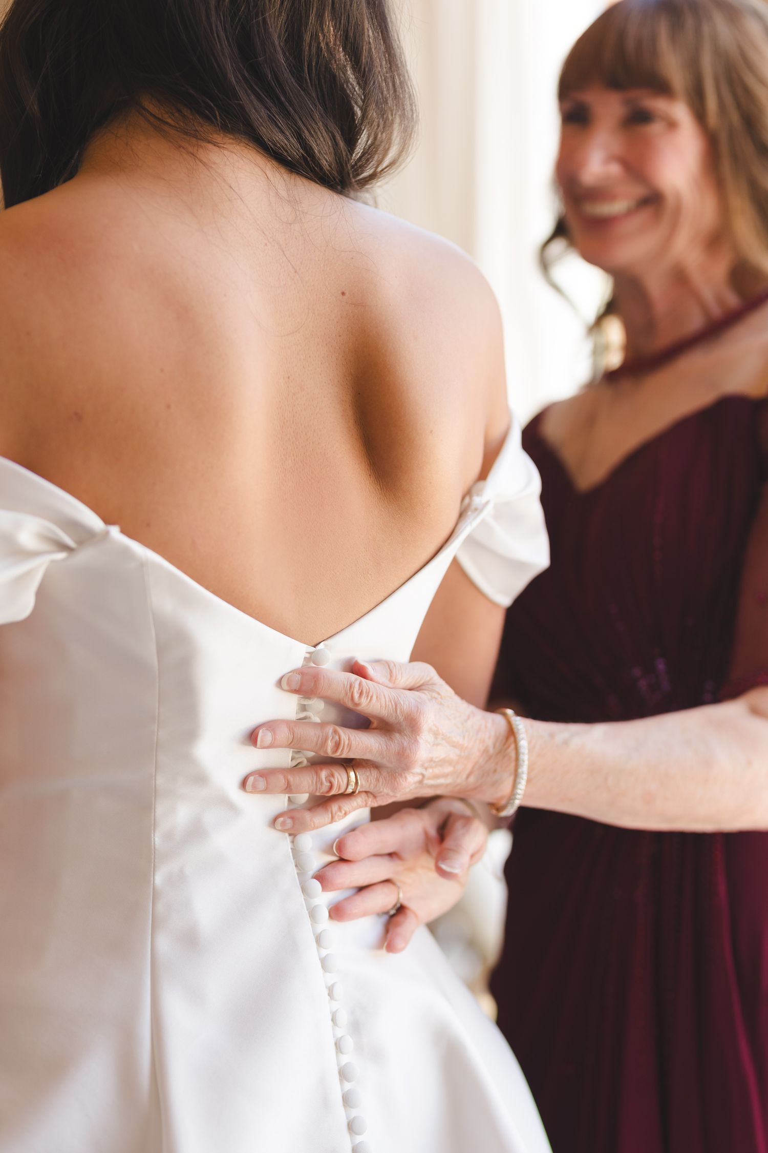 Close-up of wedding dress being adjusted showing delicate white fabric details.