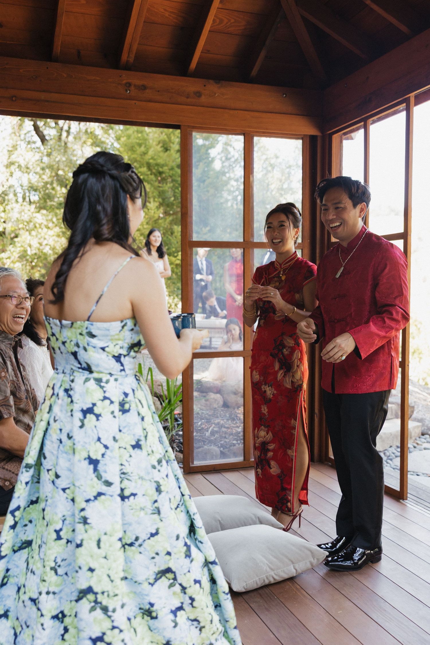 People in formal attire gather on a screened porch, with a woman wearing a blue floral dress facing others in traditional dress.