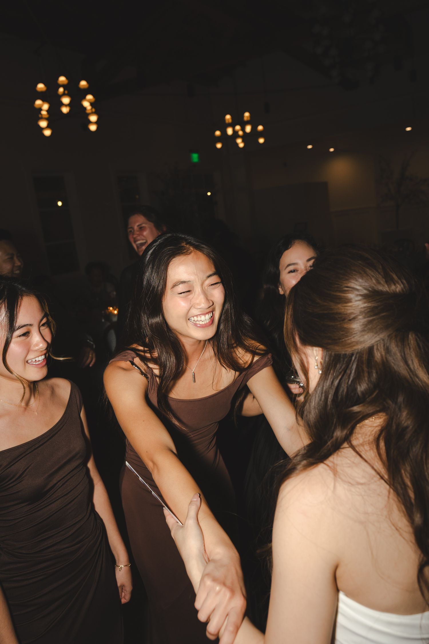 People dancing and laughing together in a dark venue with twinkling lights in the background.