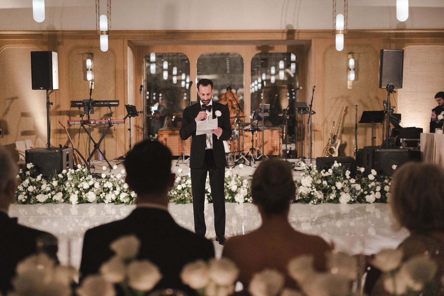 A wedding ceremony in progress with musical instruments on stage and white floral arrangements decorating the elegant venue.