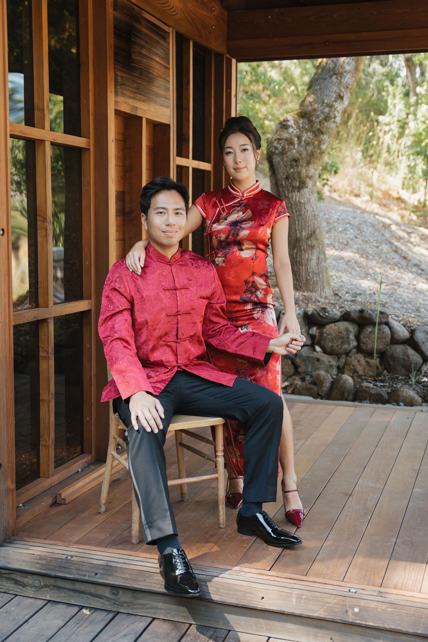 A person in a red traditional Chinese jacket sits on a wooden deck with a scenic backdrop.