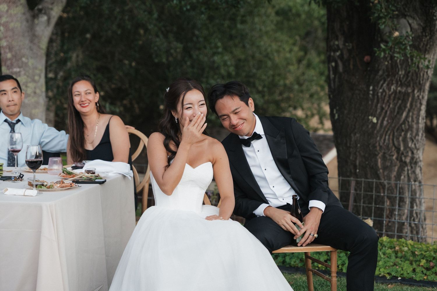 Candid reception moment of wedding couple laughing at outdoor table.