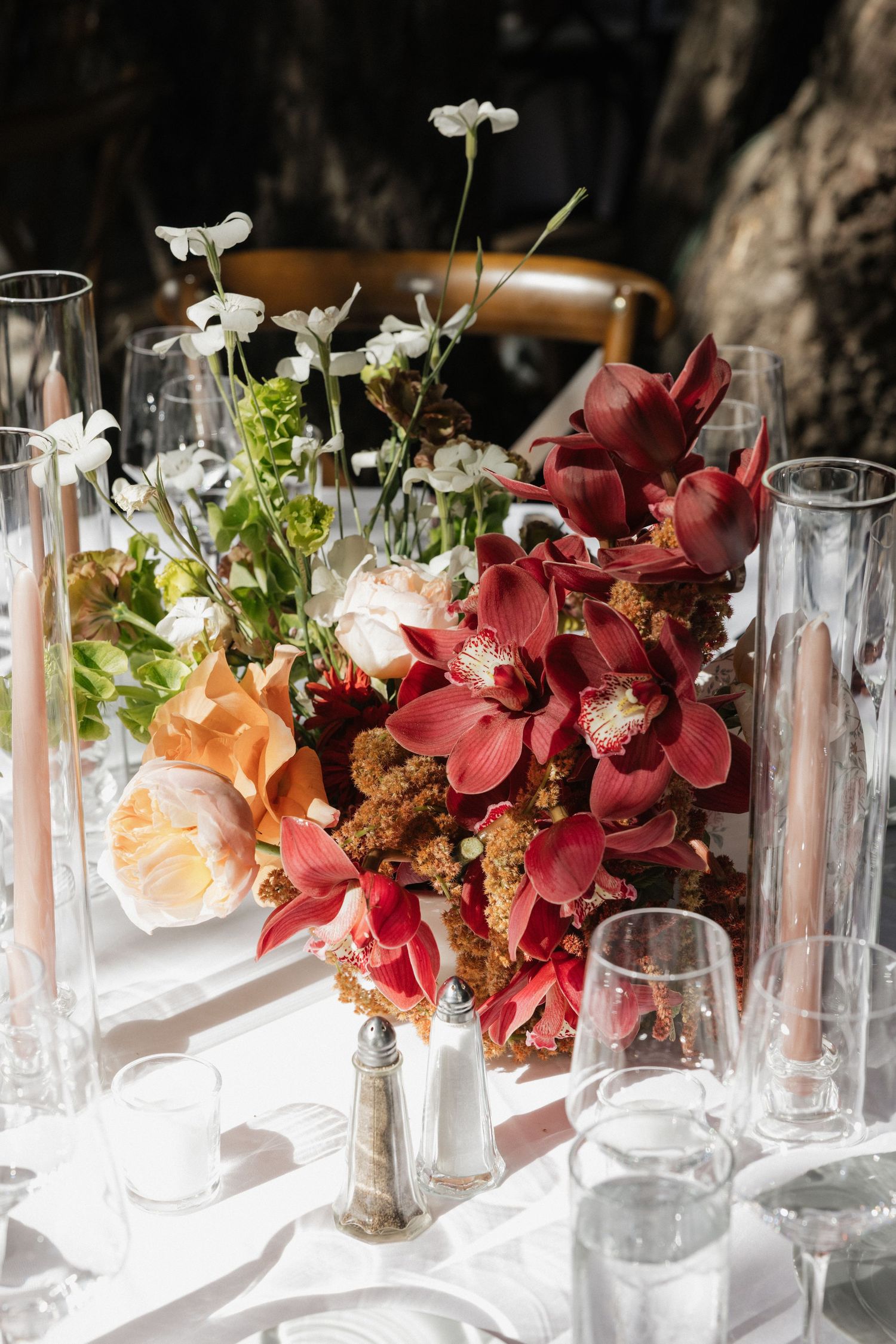 Elegant wedding table centerpiece featuring deep red orchids, white flowers, and tall glass candle holders.
