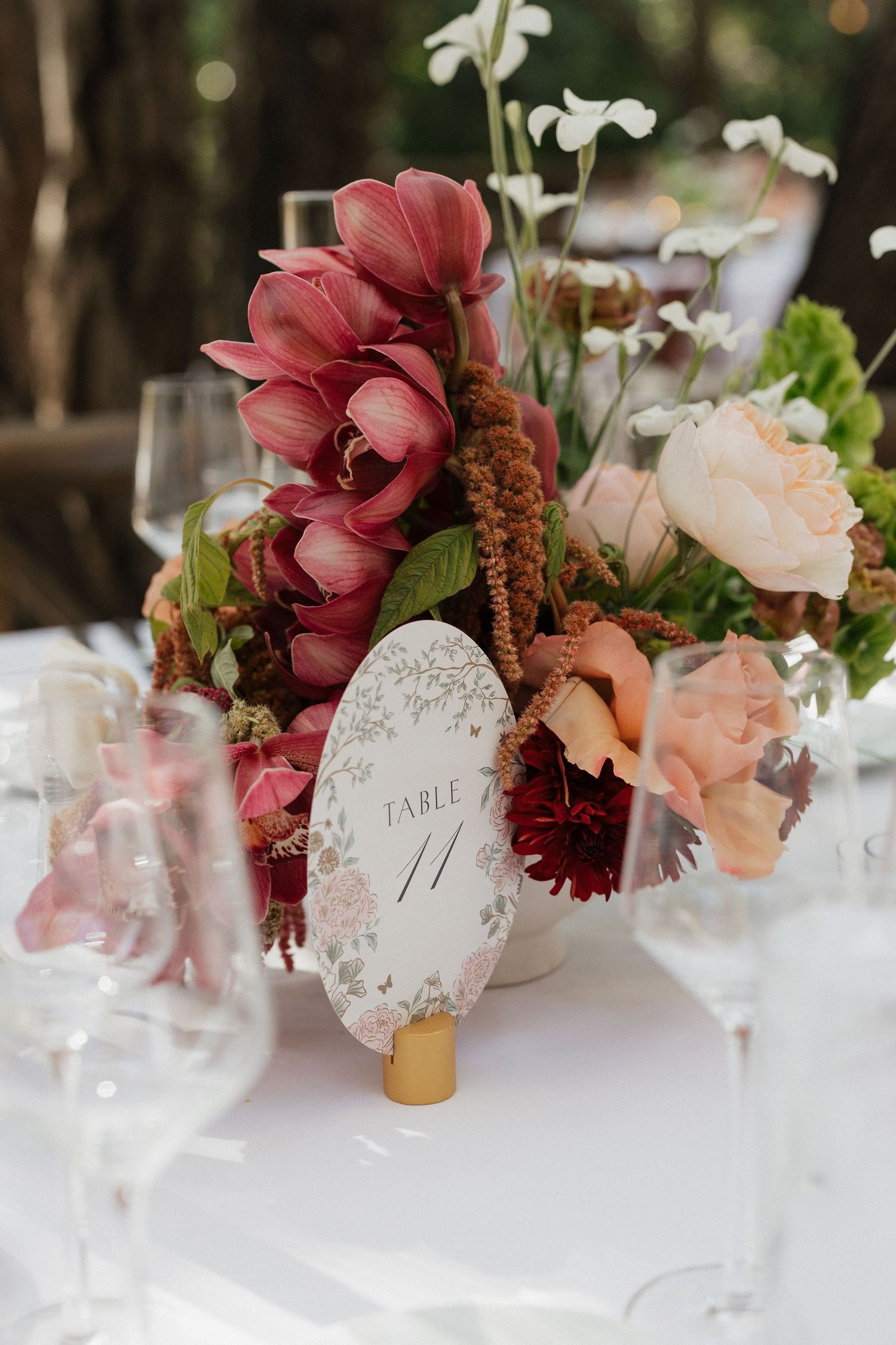 Elegant wedding table centerpiece with pink and burgundy flowers, peach roses, and a Table 11 card on white linen.