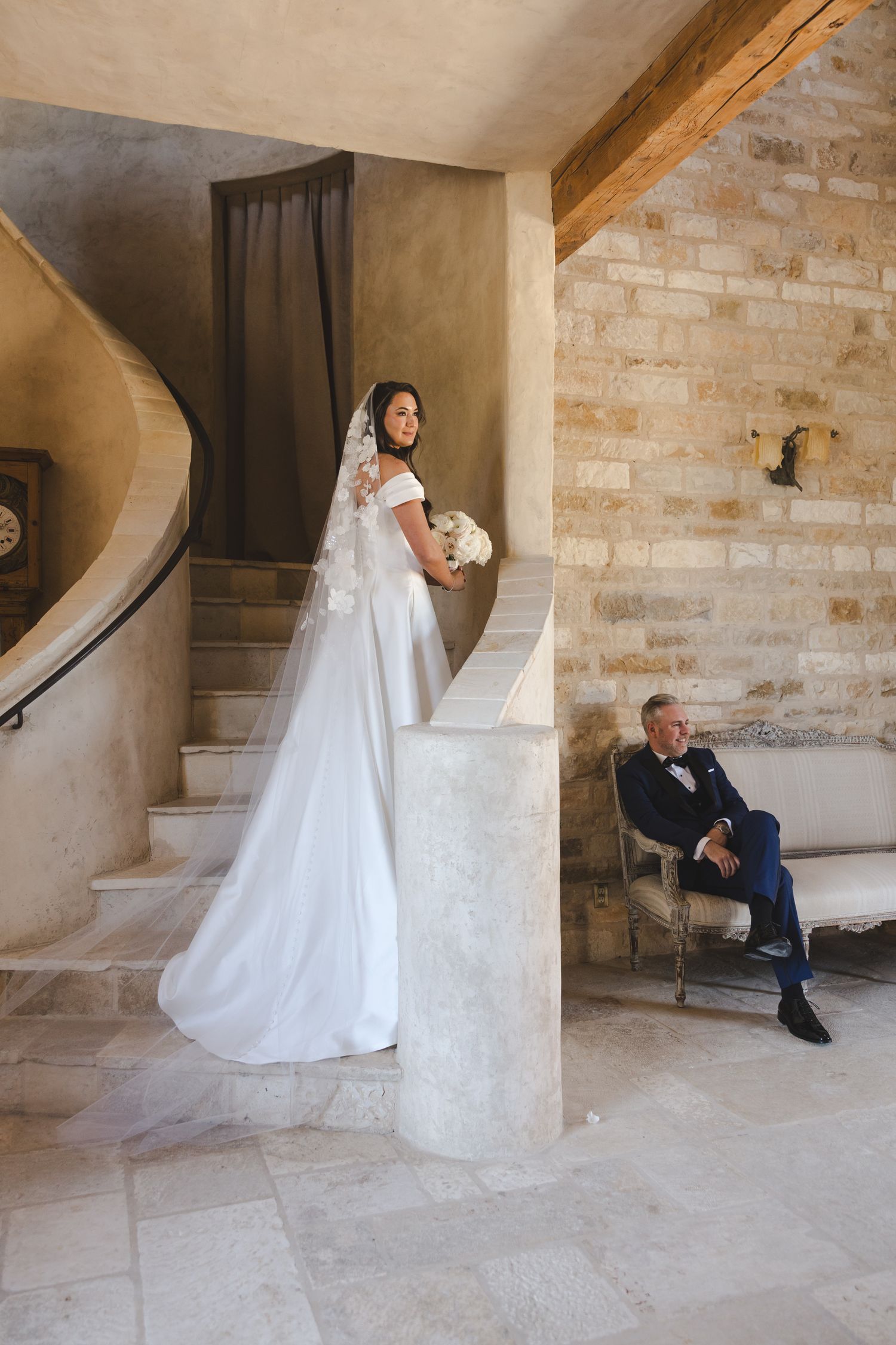 Elegantly captured wedding moments of a couple posing against stone walls on a grand staircase with natural lighting.