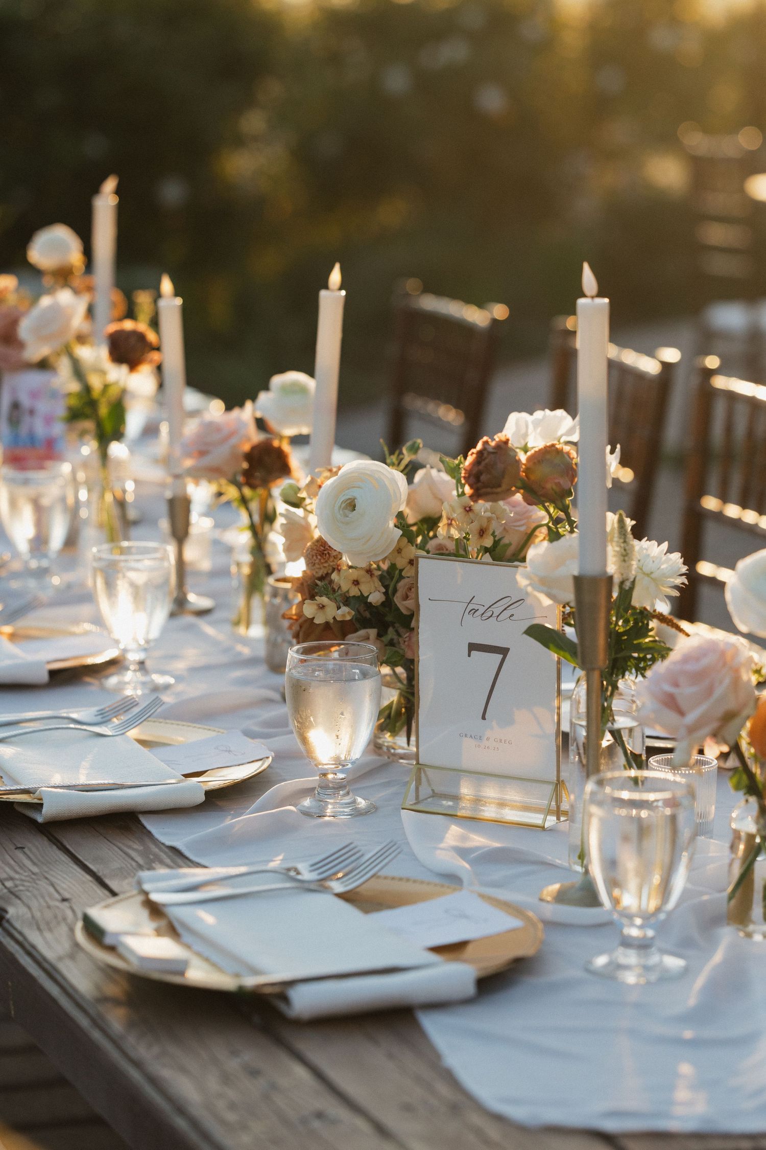 Elegant wedding table setting with candles, flowers and place cards at sunset.
