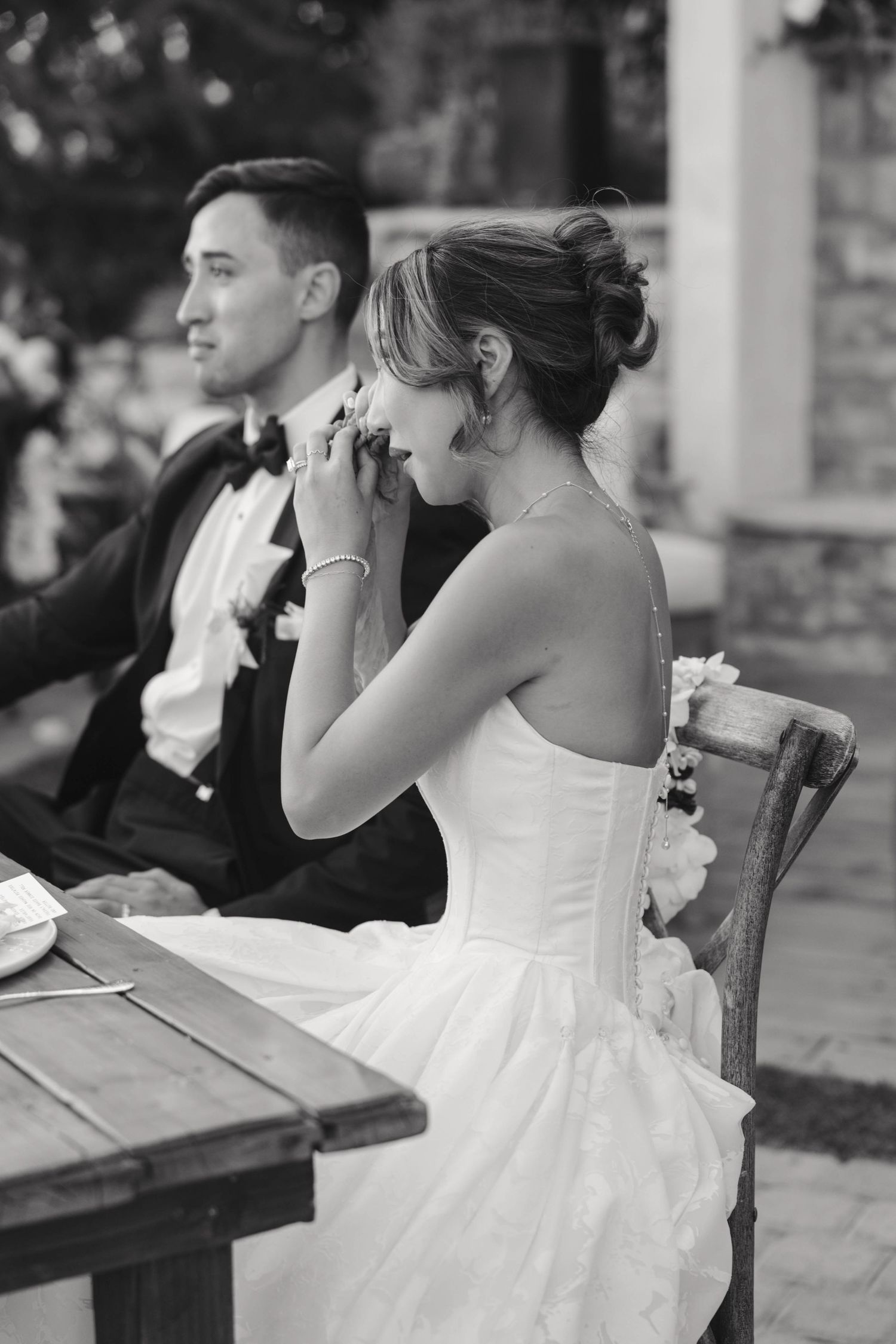 A black and white candid moment captured during a wedding reception at an outdoor venue.