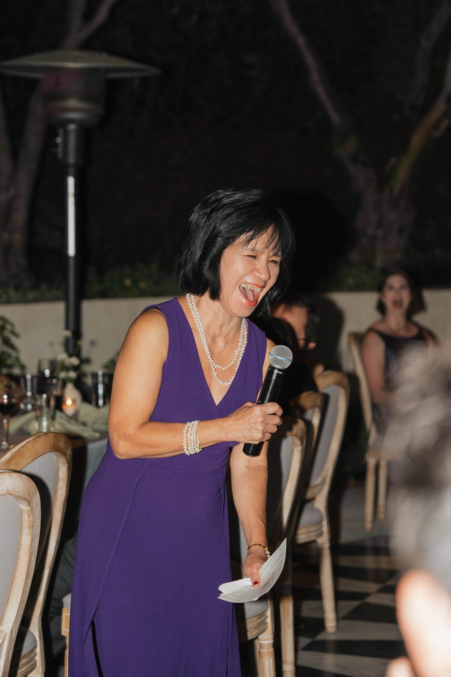 Woman in purple dress giving speech at outdoor evening event.