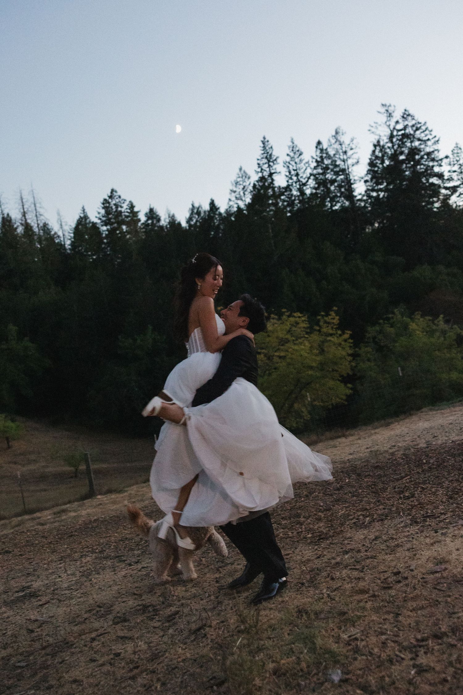 Romantic outdoor photoshoot with couple spinning on hillside at dusk.