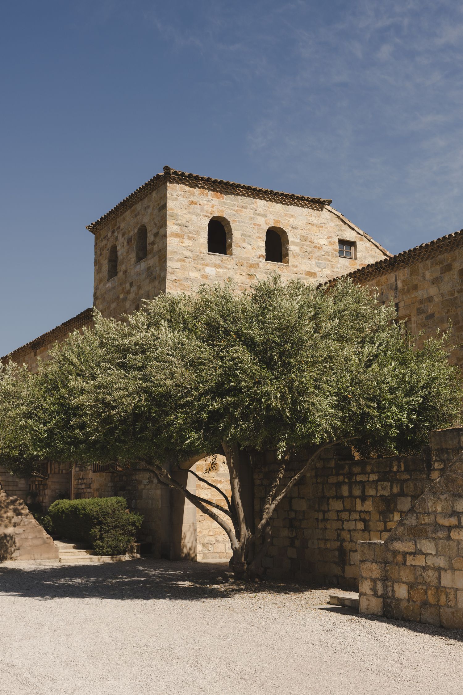 A rustic stone building with arched windows and a Mediterranean architectural style surrounded by olive trees.