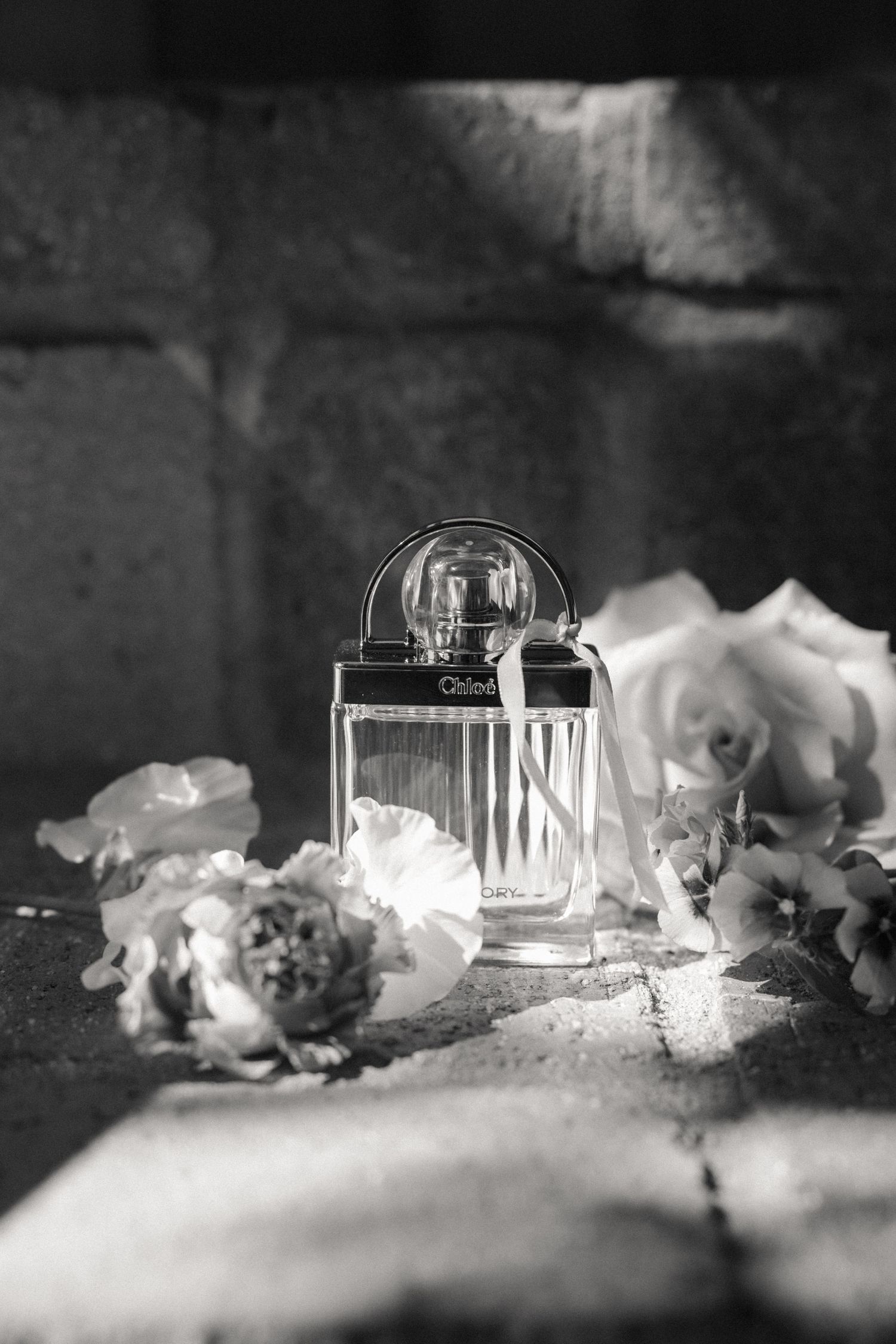 Black and white close-up of wedding decorations with delicate flowers and glassware on a textured surface.