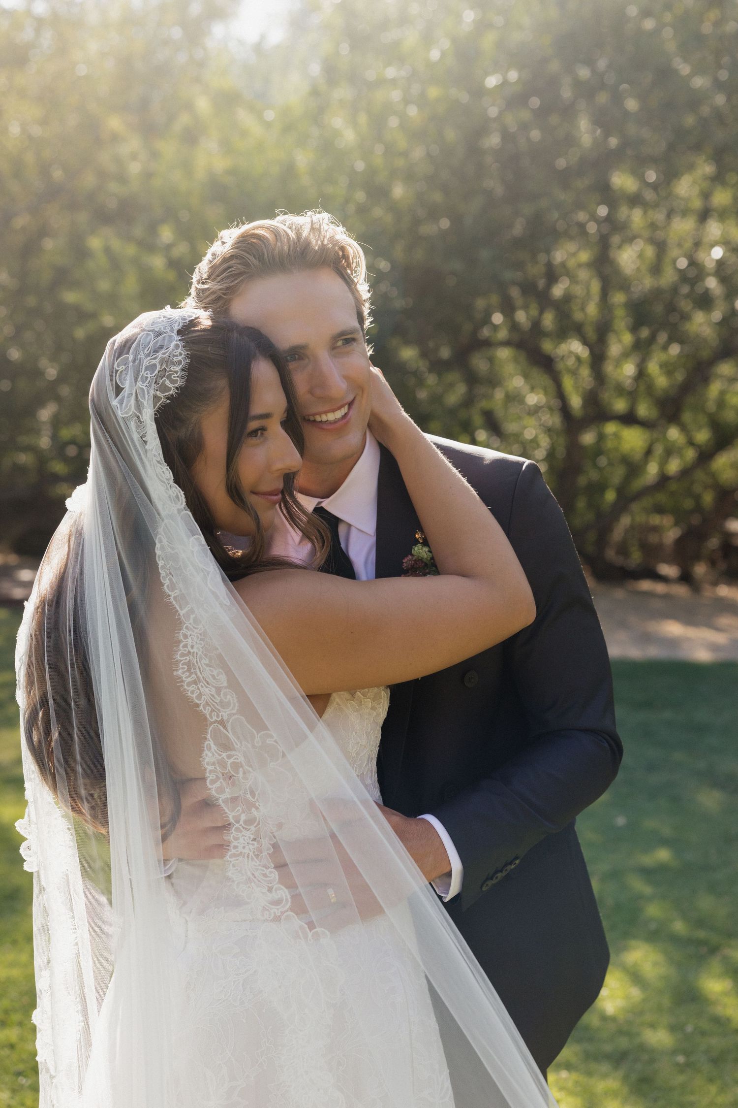 Joyful bride and groom embracing and laughing together outdoors in golden sunlight after wedding.