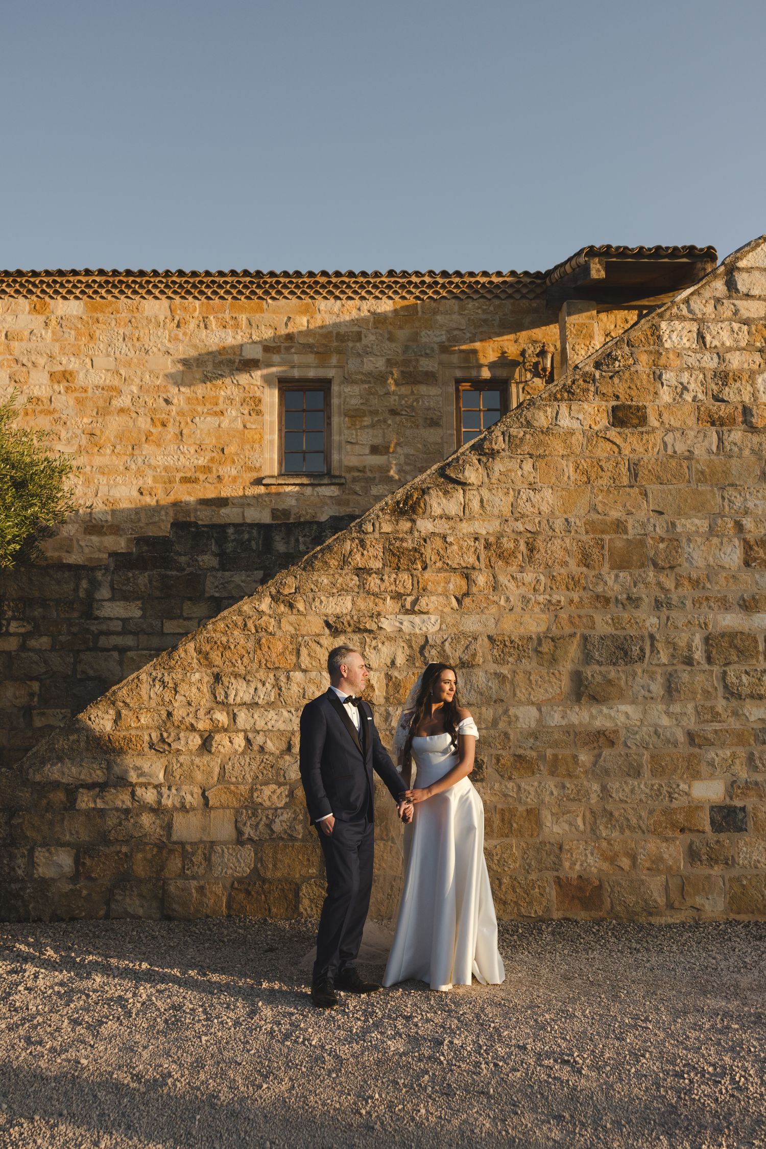 Wedding couple poses against rustic stone wall at a winery.