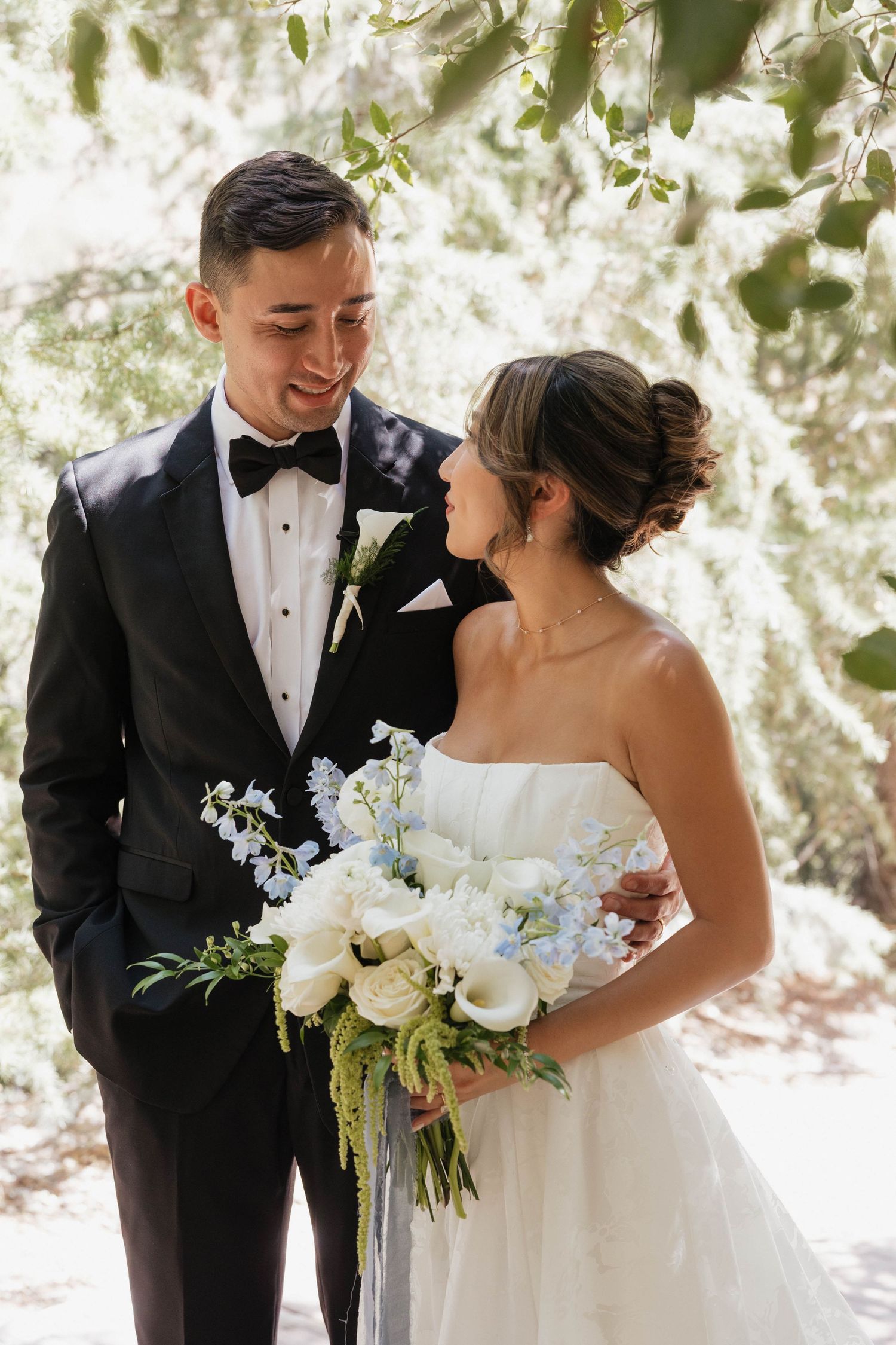 Wedding couple sharing a joyful moment together outdoors with white floral bouquet.