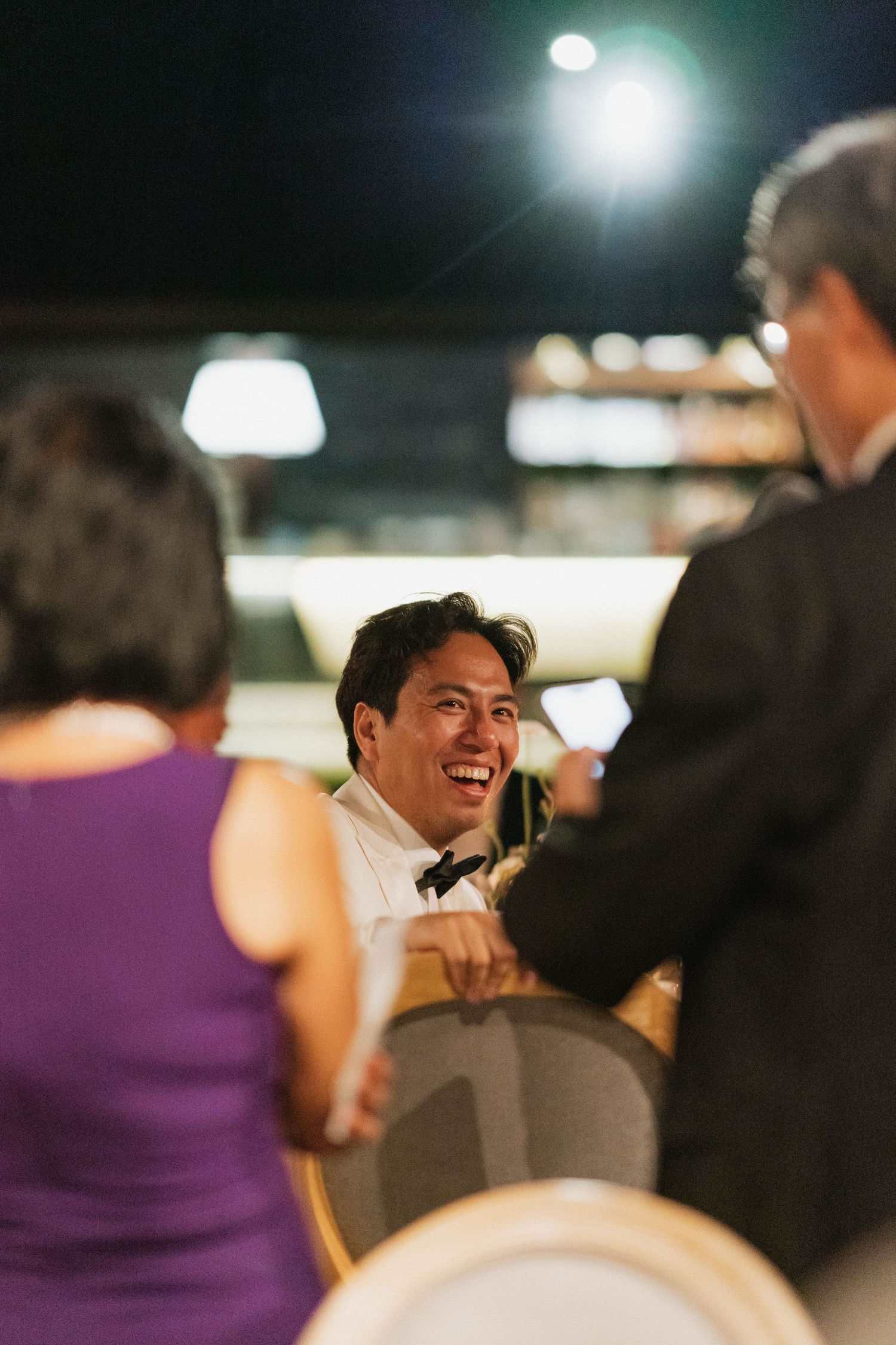 A guest in formal attire shares a laugh during an evening reception.