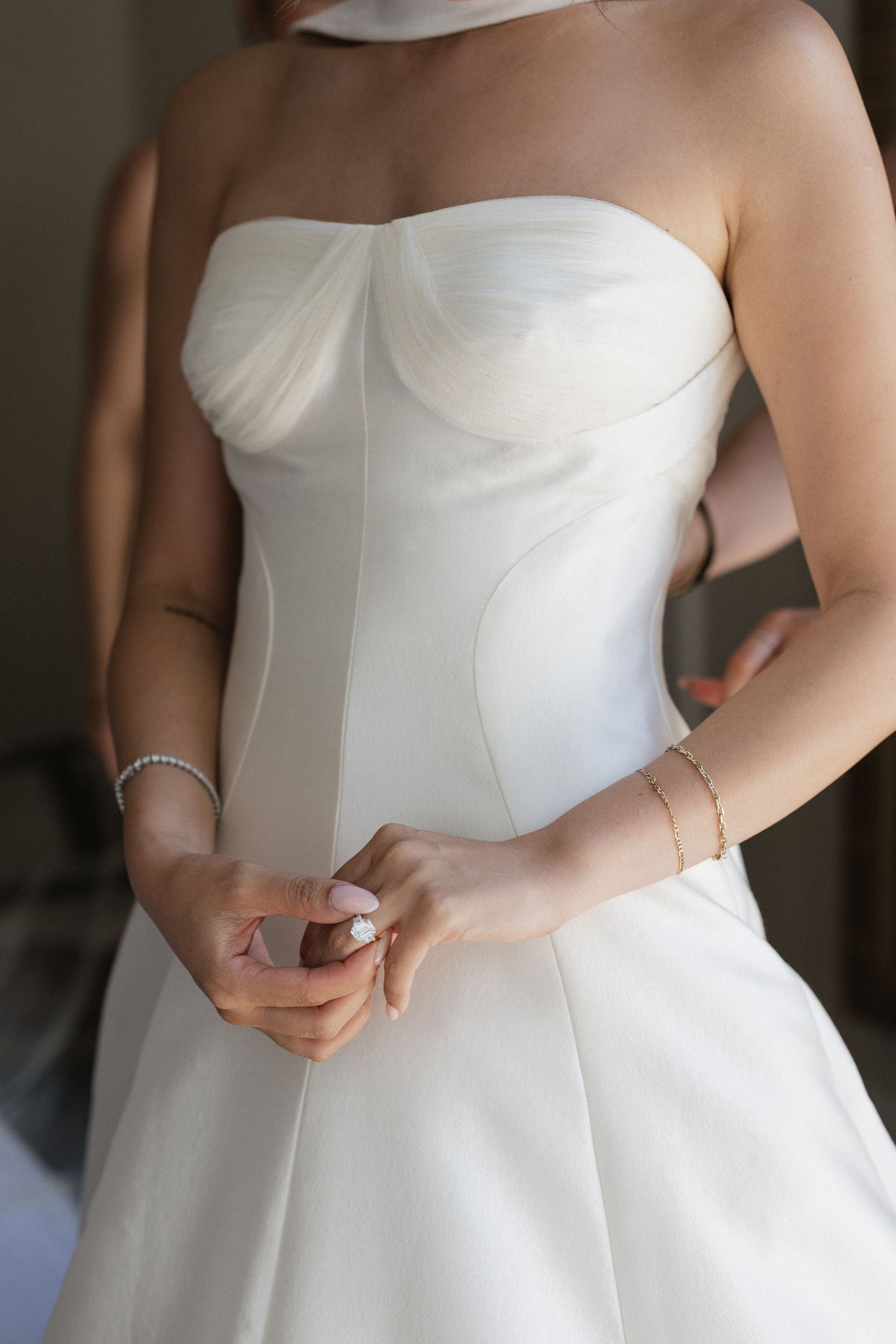Bride in strapless white corset wedding dress with bracelet and ring, hands clasped at waist.