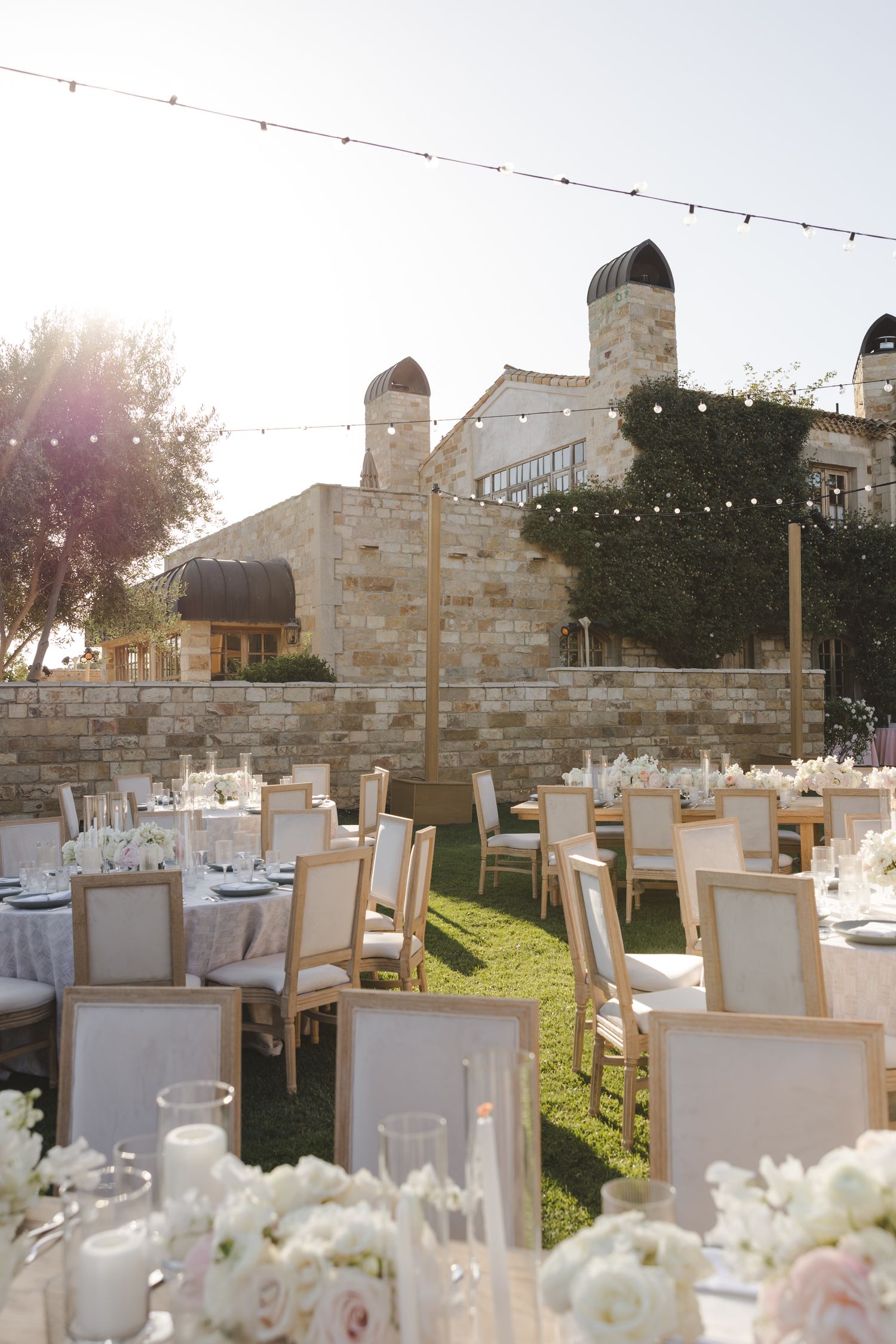 Elegant outdoor wedding reception setup with string lights and white chairs at sunset.