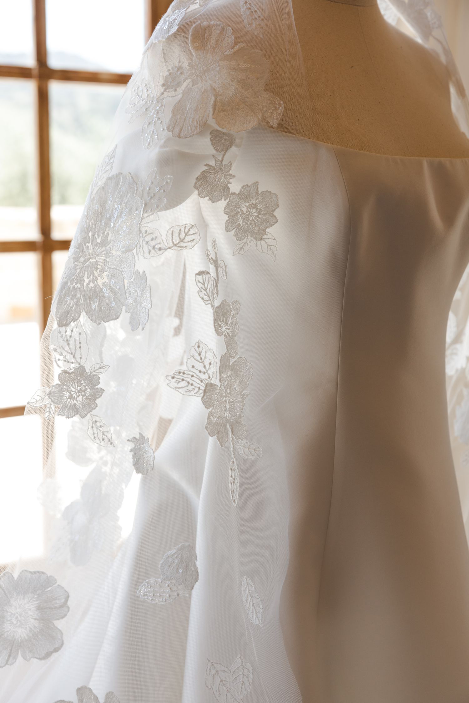 Close-up detail of white wedding dress with delicate floral lace embellishments.