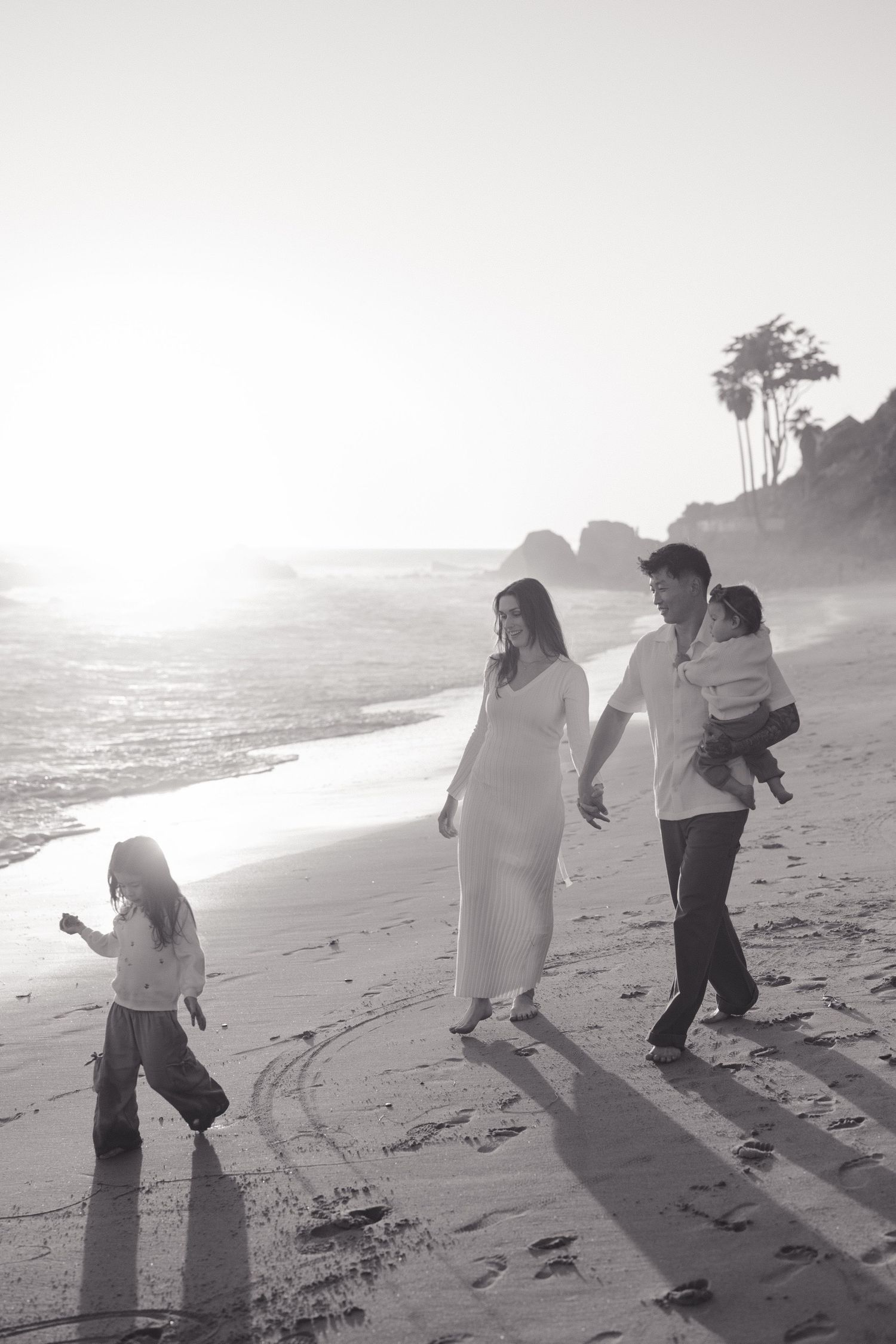 A family walks together along a misty beach at sunset, casting long shadows on the sand.