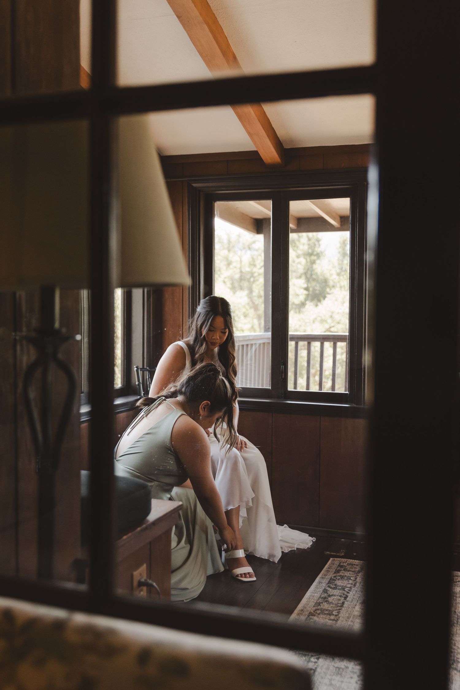 A figure in a white gown gets ready in a rustic wooden room, viewed through a decorative frame.