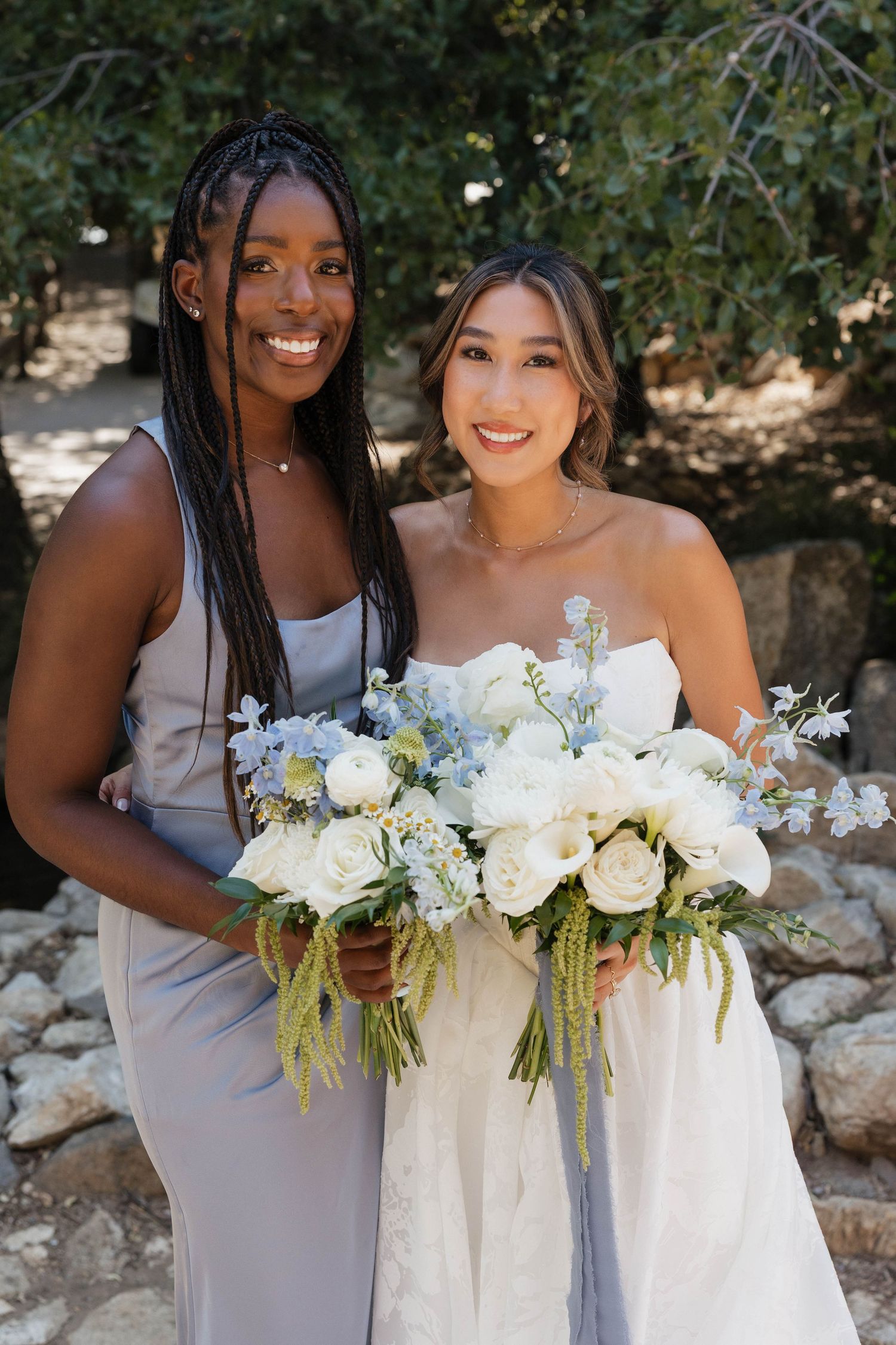 Bridesmaids in grey dresses hold white floral bouquets while posing with bride outdoors.