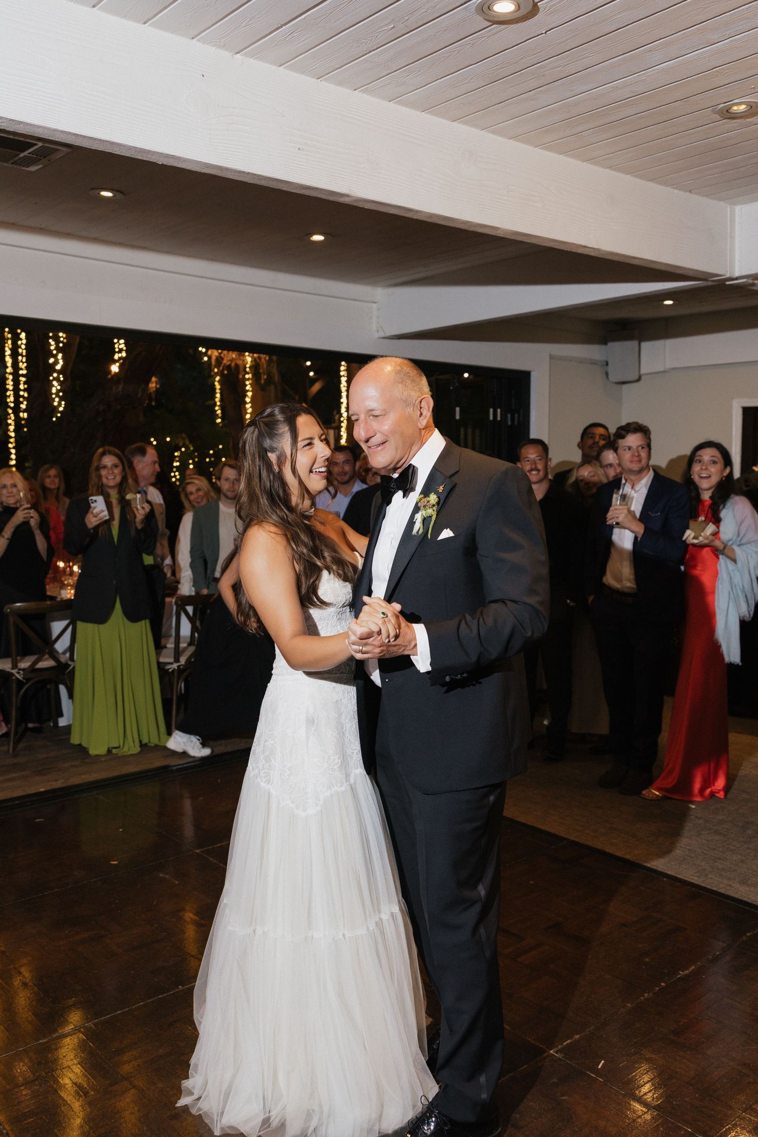 Bride shares emotional father-daughter dance at wedding reception surrounded by celebrating guests.
