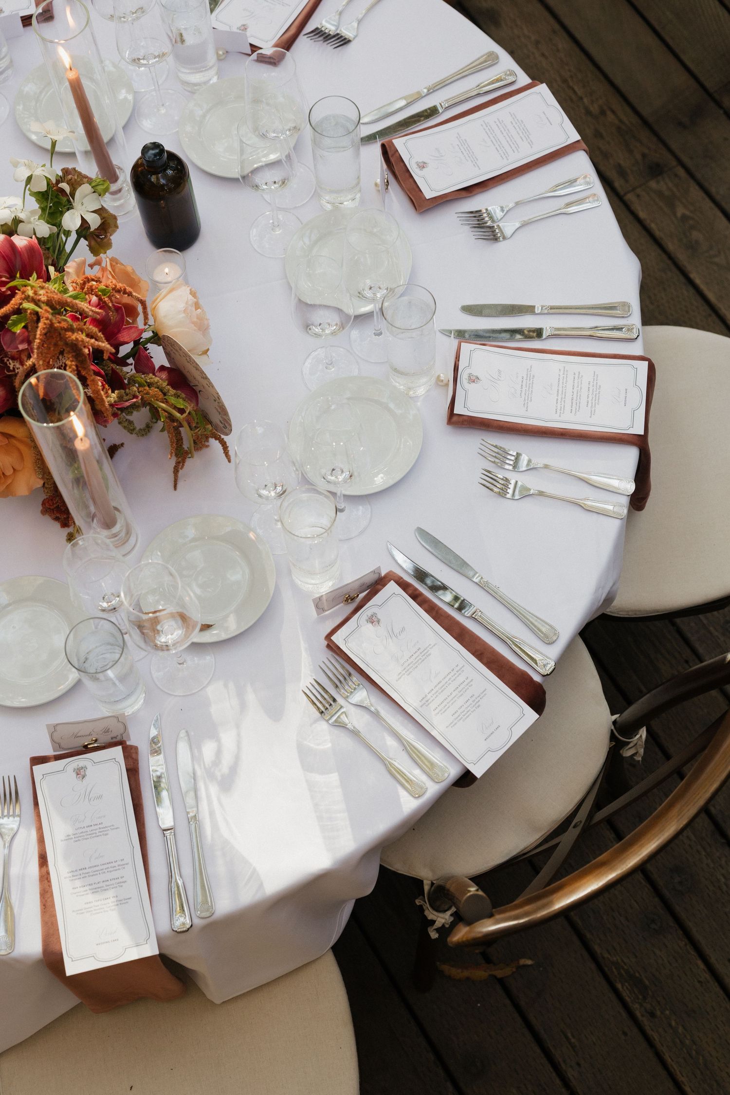 Overhead view of elegant round wedding reception table with white linens, place settings, menus, and floral centerpiece.