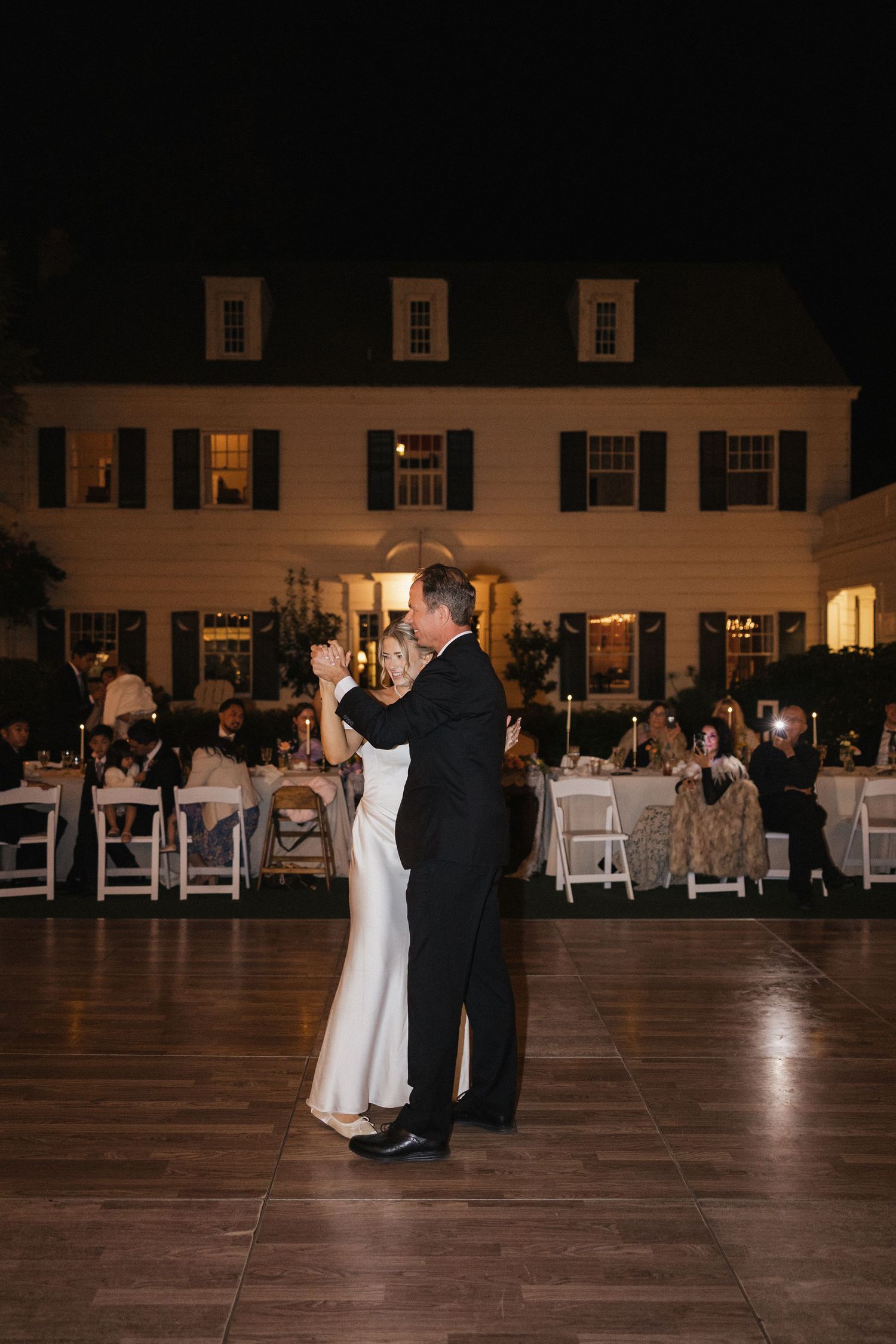 Couple sharing their first dance on a spacious wooden floor at an evening wedding reception.