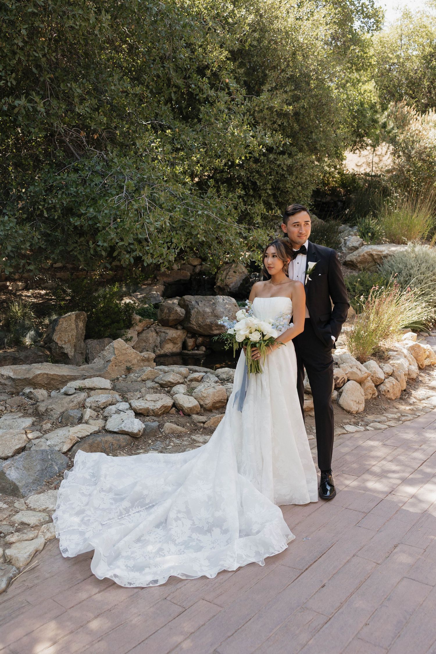 Wedding couple posing on brick pathway with flowing white dress train.