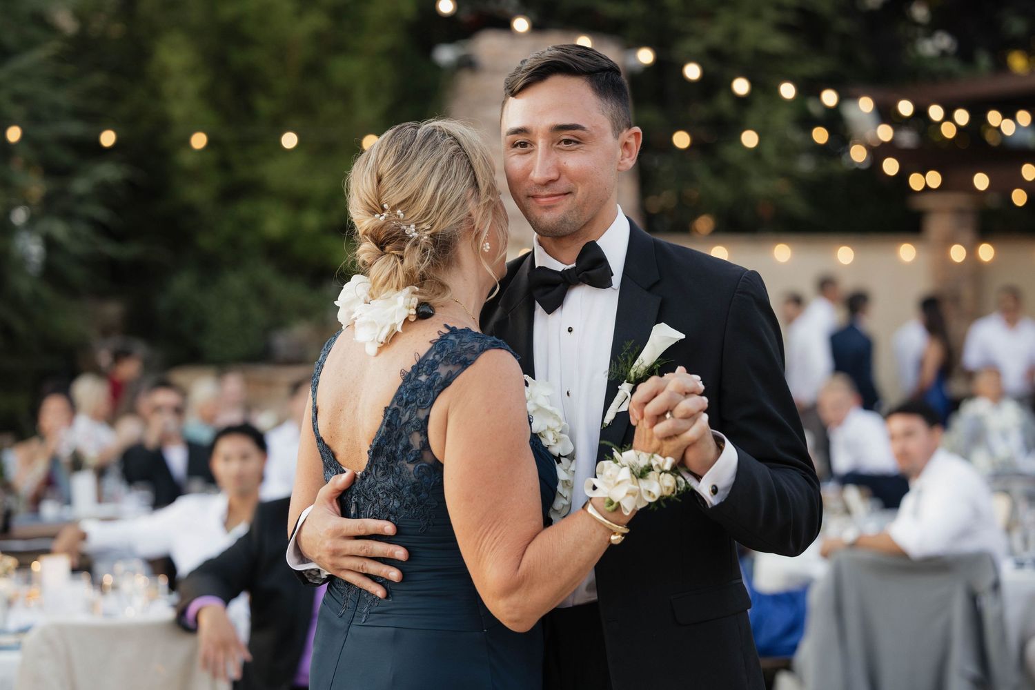 A wedding couple dances together during an outdoor evening reception beneath string lights and decorations.