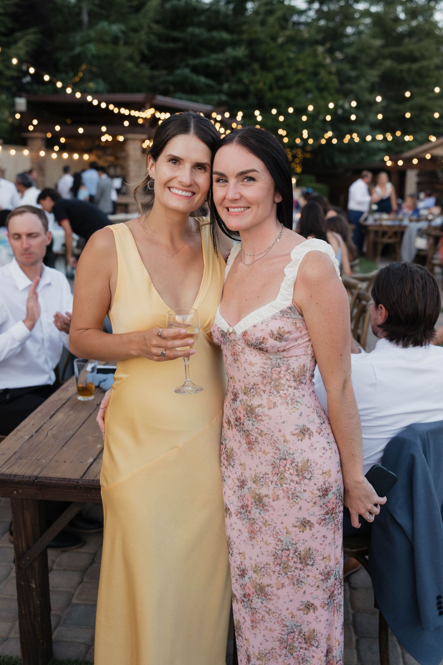 Wedding guests in summer attire enjoying drinks at an outdoor evening reception.