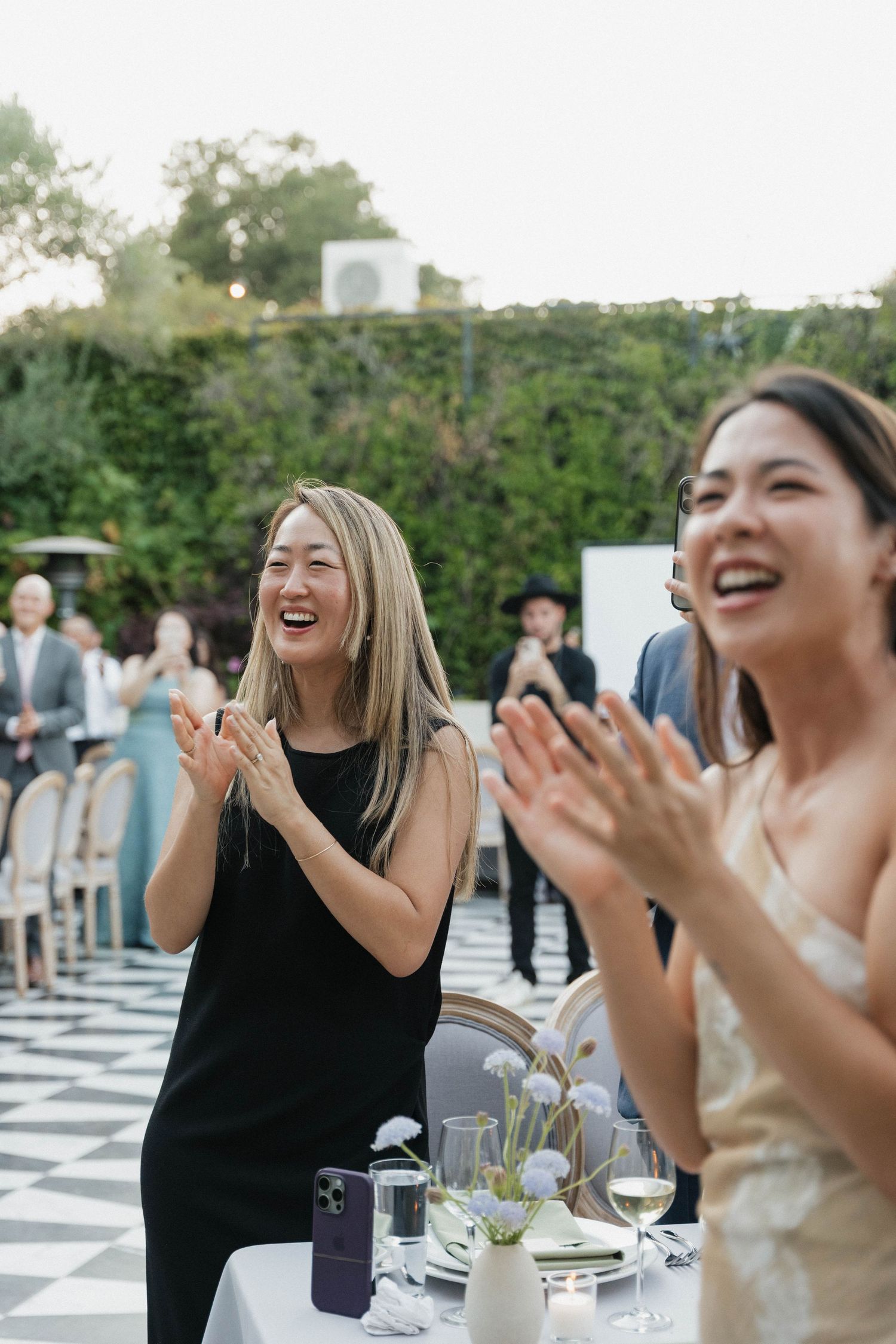 People at an outdoor reception table laughing and clapping during a joyful celebration.