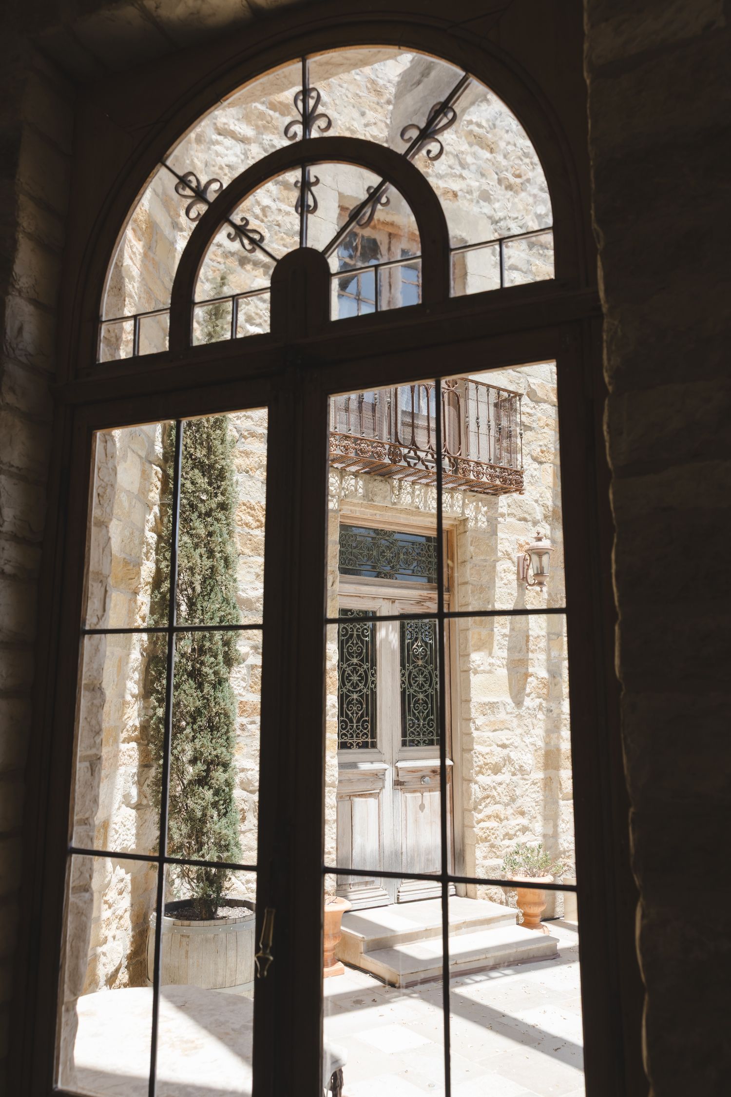 View through arched doorway showing stone walls, ornate iron details and sunlit courtyard of a Mediterranean building.