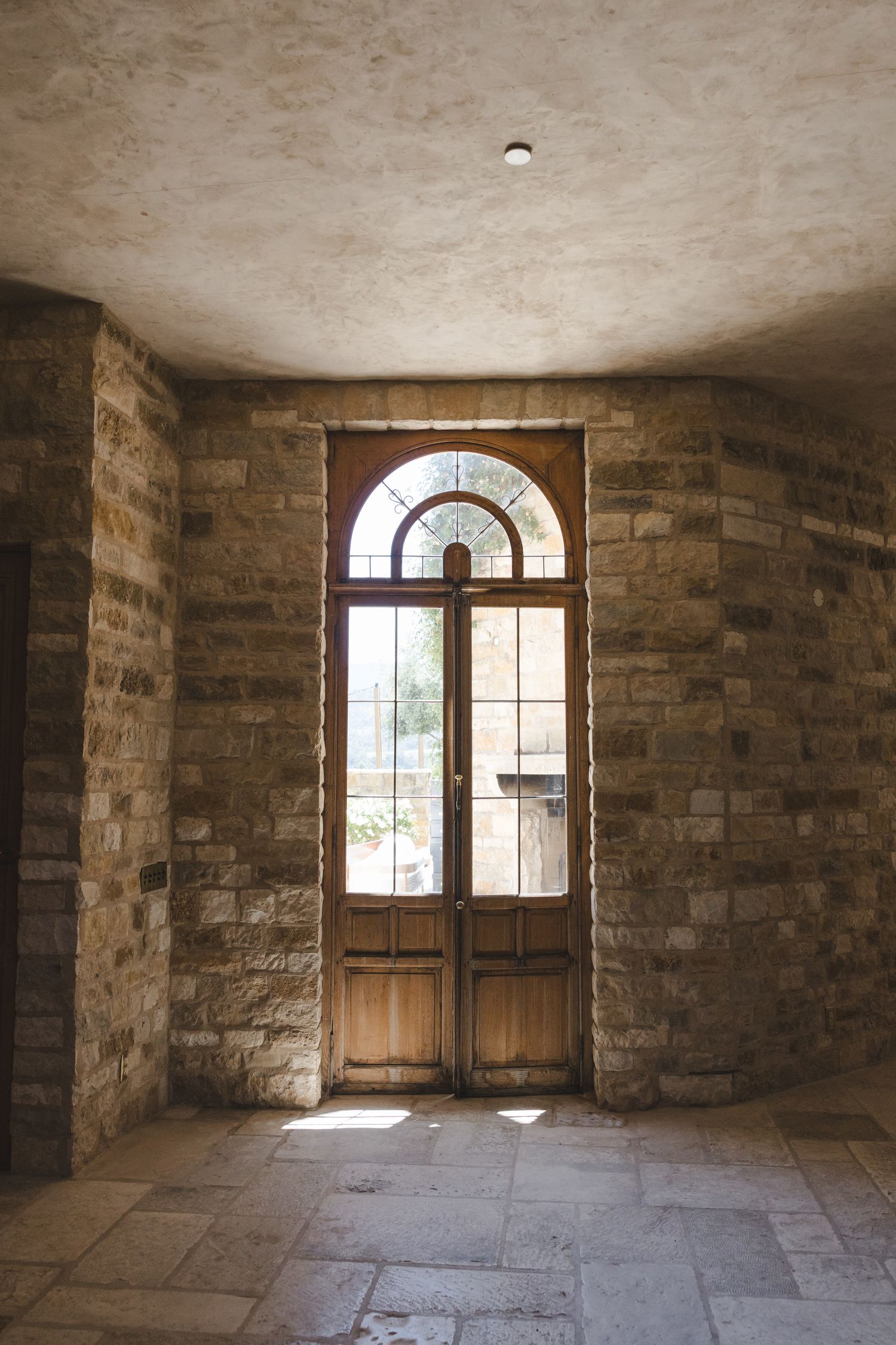 Rustic stone archway with arched wooden door and natural light streaming through.