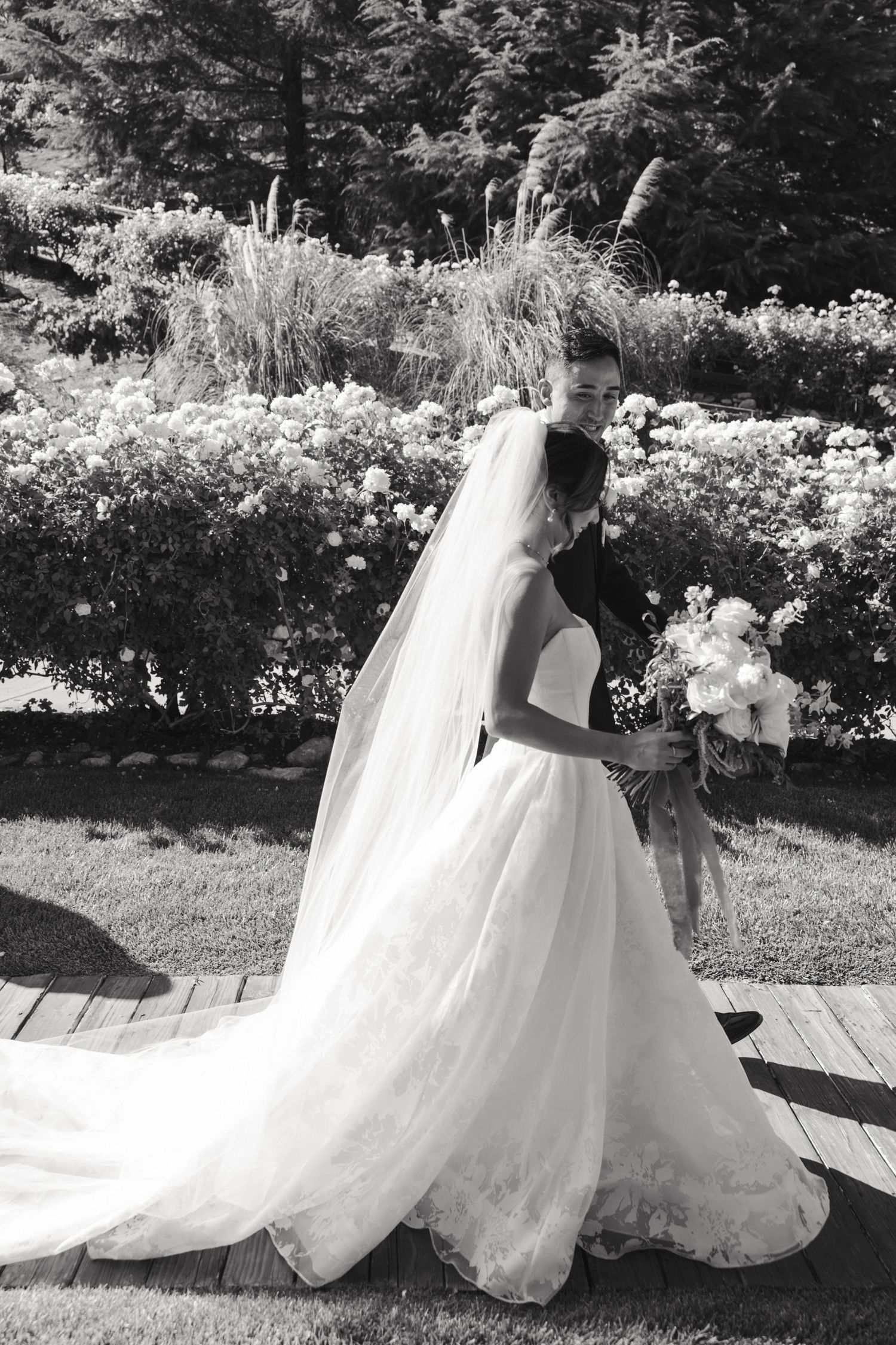 Black and white portrait of bride in full skirt wedding gown with bouquet in garden setting.