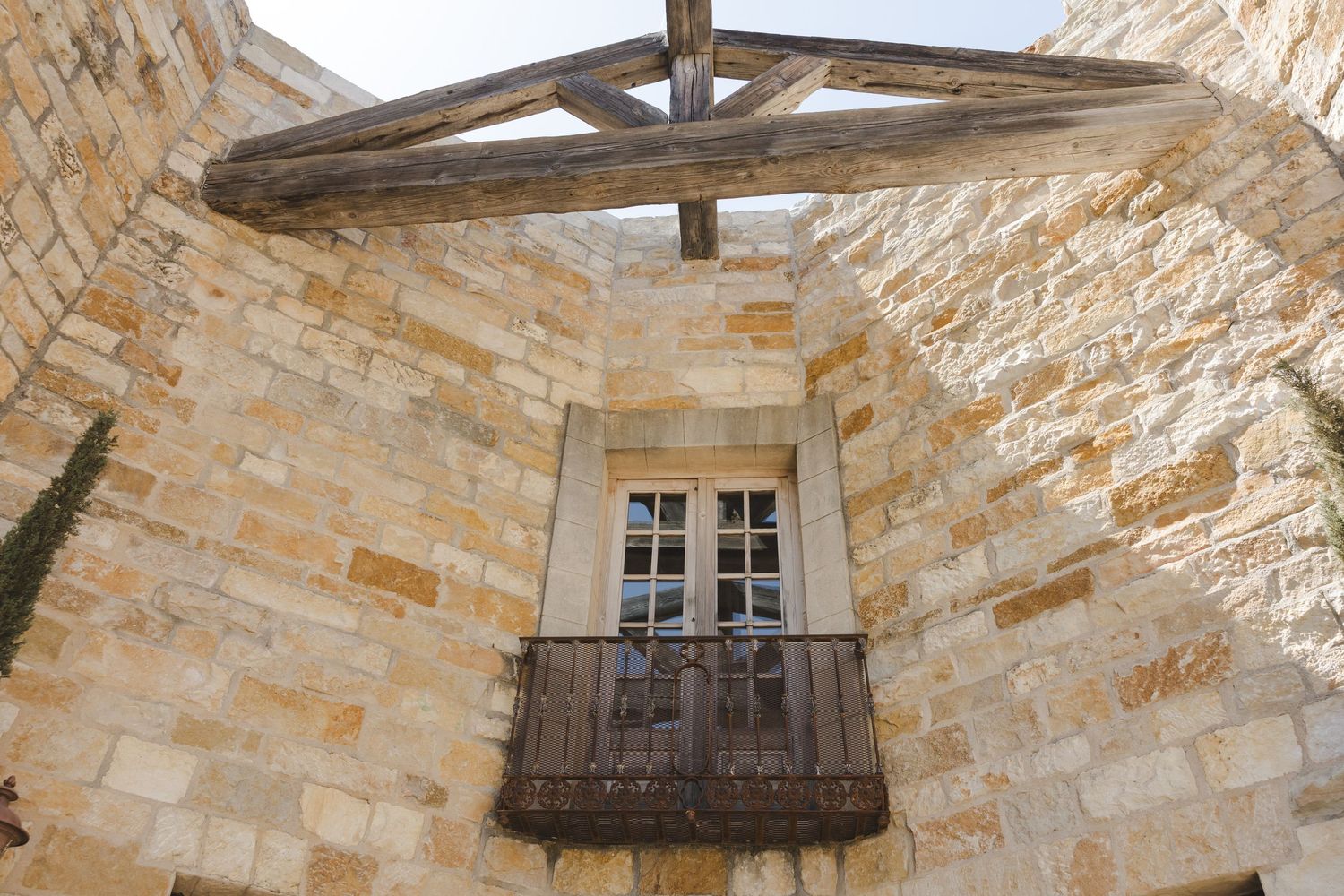 Old rustic balcony with weathered wooden shutters on beige stone building facade in Mediterranean architecture style.
