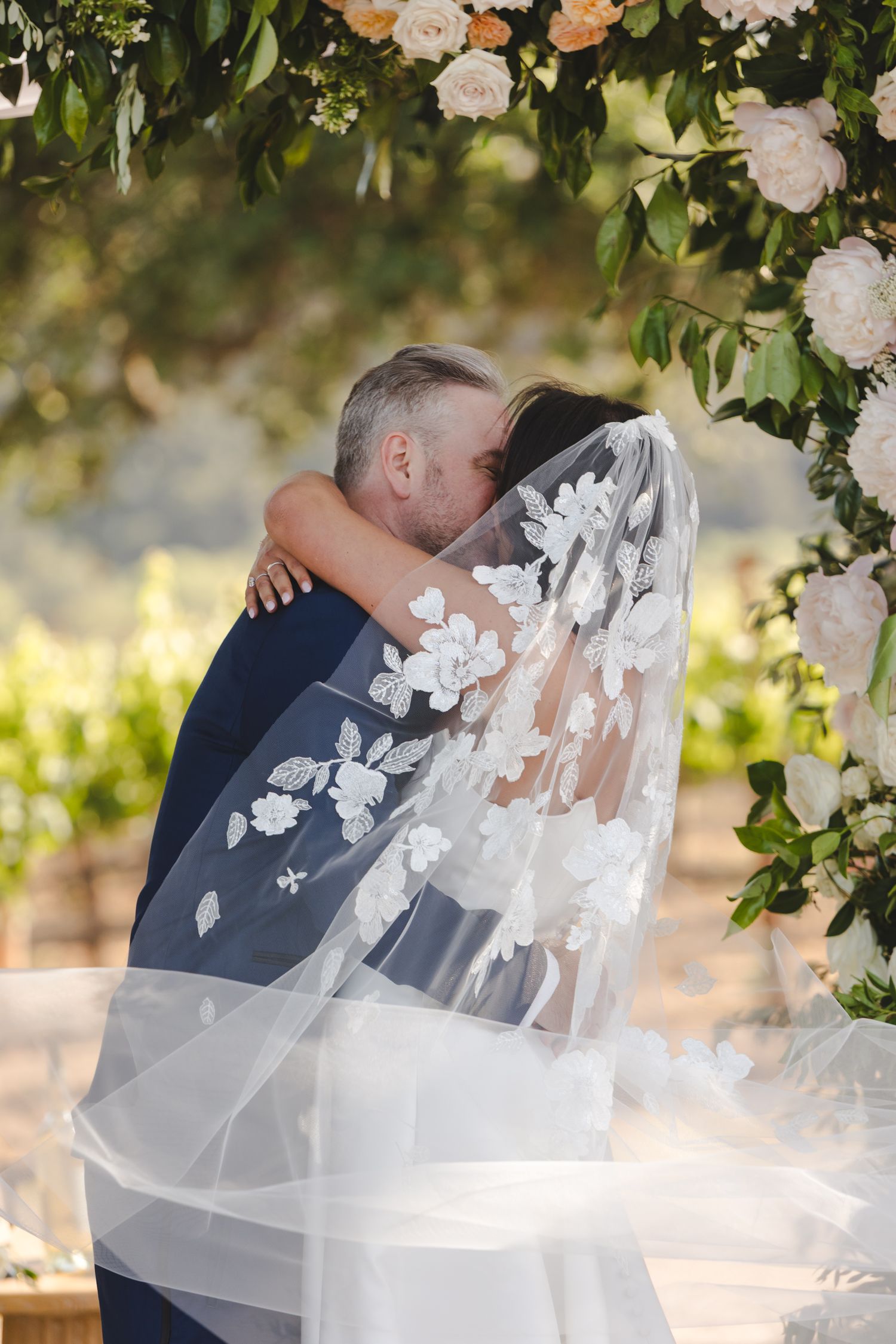 Intimate wedding moment under floral archway with delicate veil details.