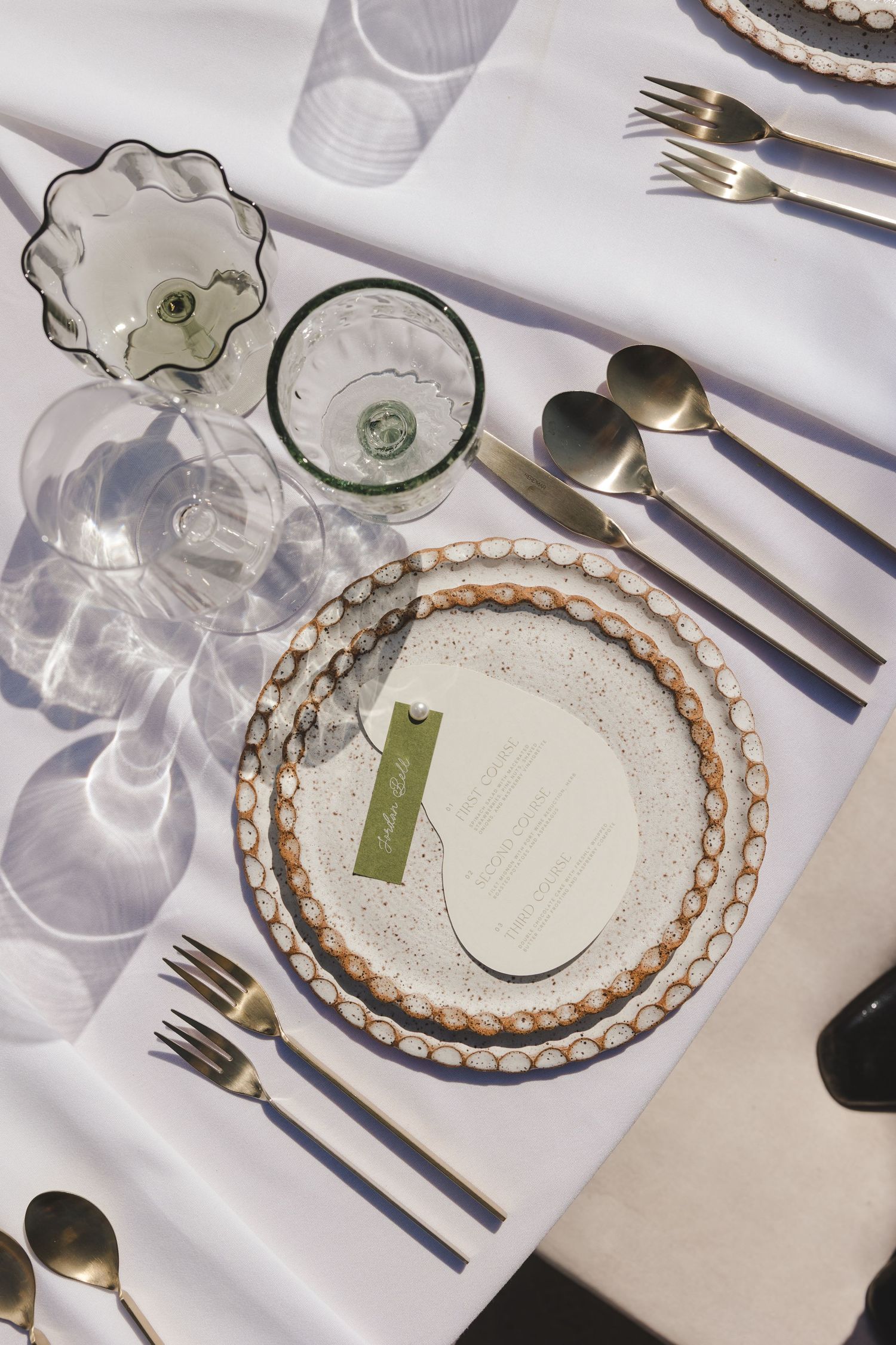 Elegant table setting with beaded charger plates, glass stemware, and silver cutlery on crisp white linens.