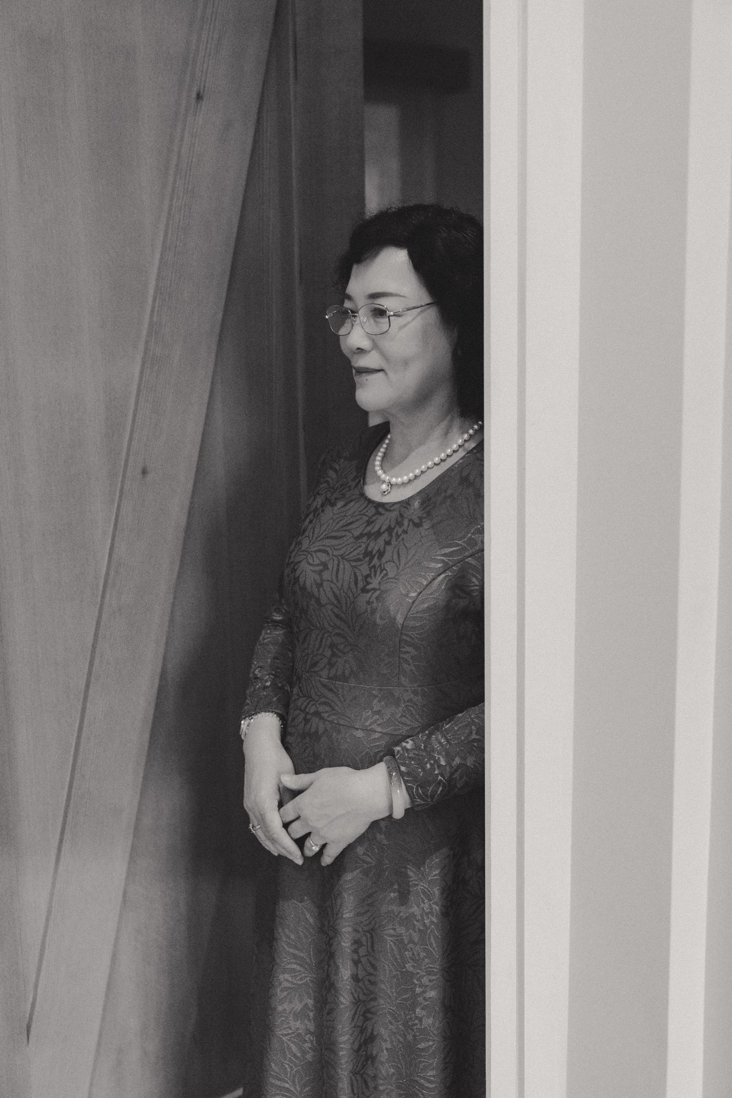 Person in formal attire standing by a window in black and white photography.