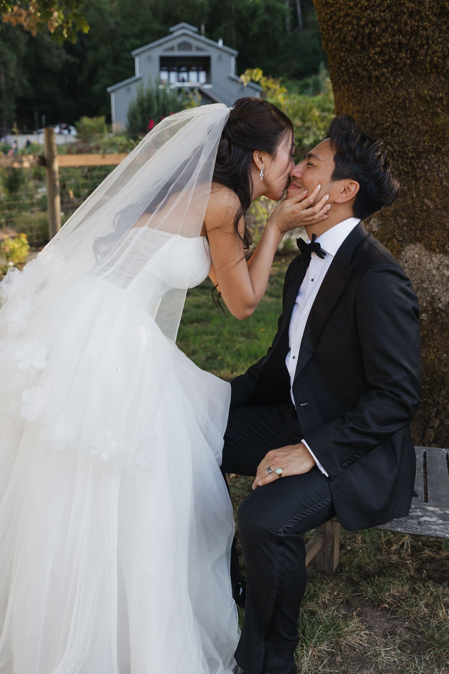 Romantic wedding couple sharing an intimate moment under trees in formal attire.