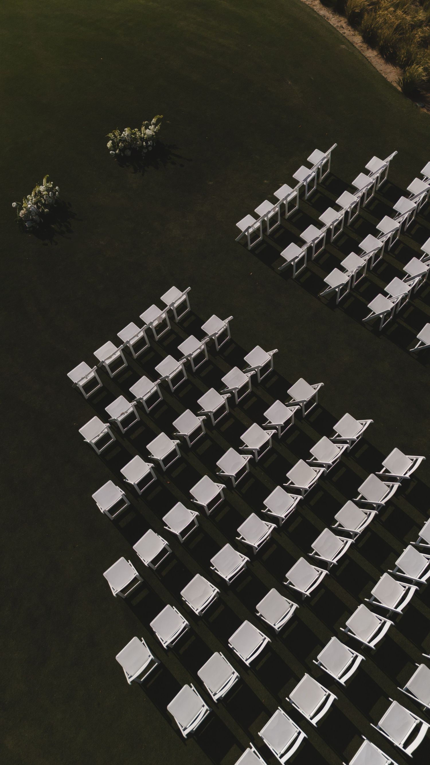 Aerial view of white chairs arranged in rows on green grass for an outdoor wedding ceremony.
