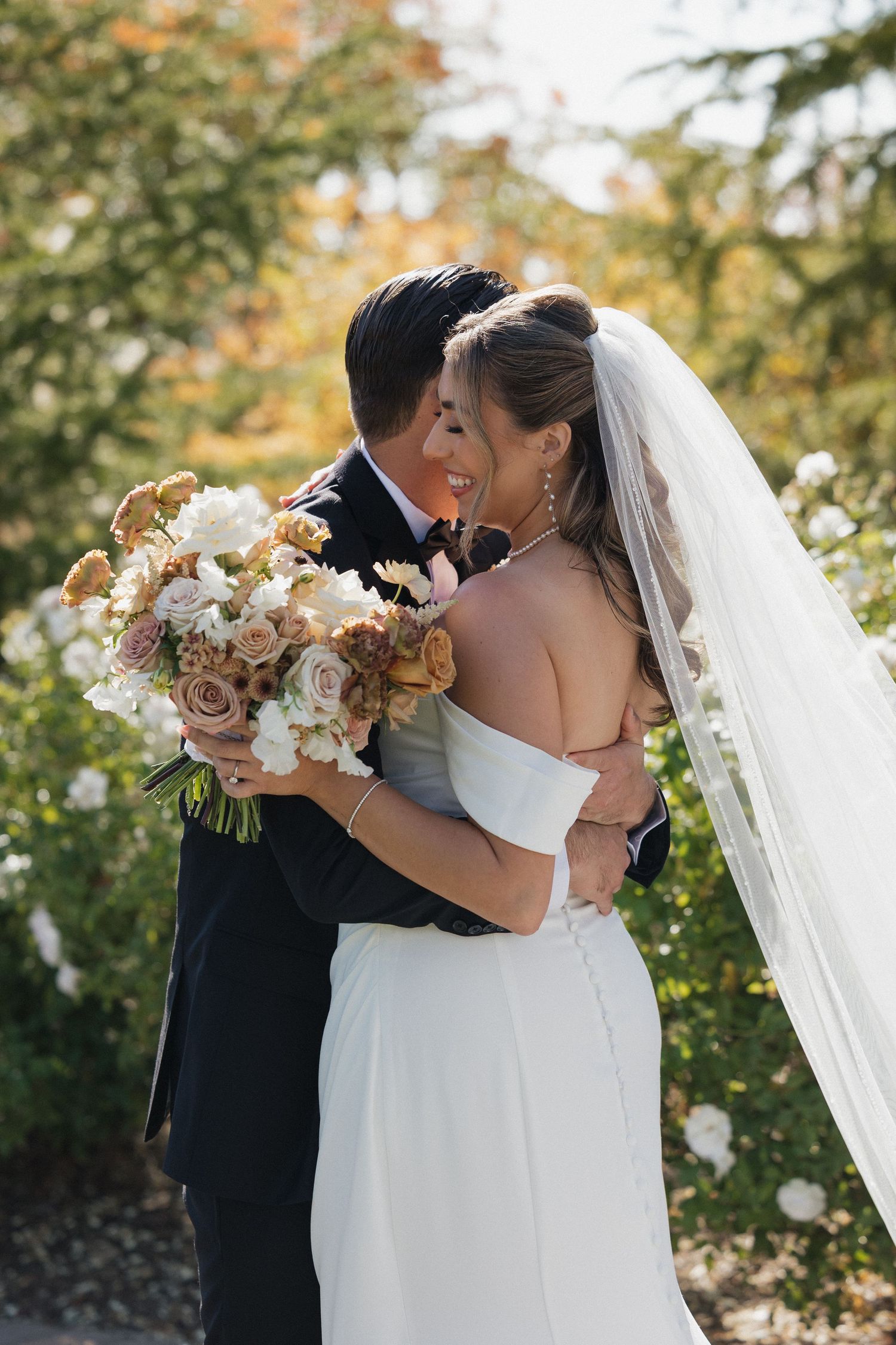 A couple shares an intimate embrace at their outdoor wedding with a beautiful autumn floral bouquet.