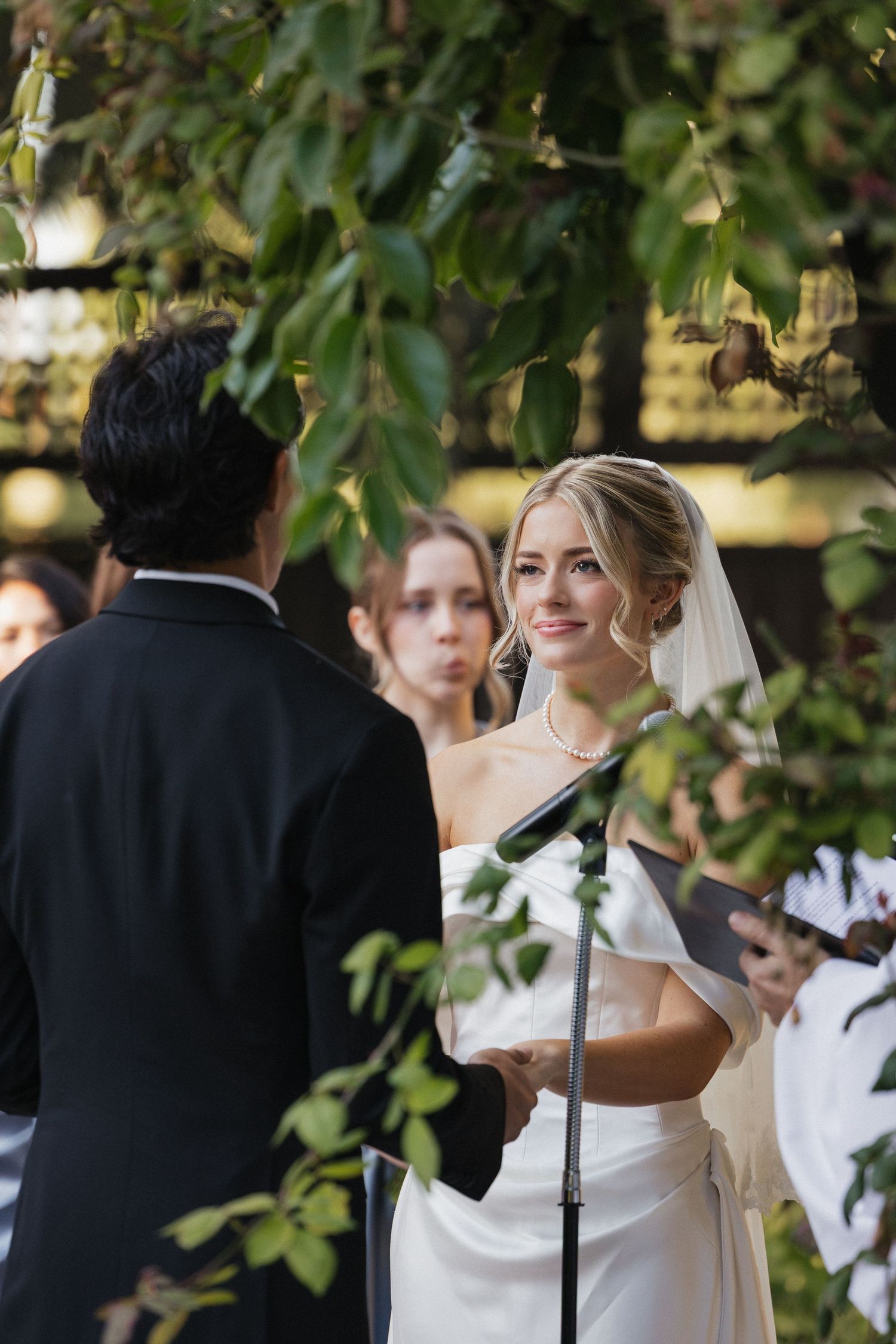 Wedding ceremony participants gathered under green foliage during an outdoor celebration.